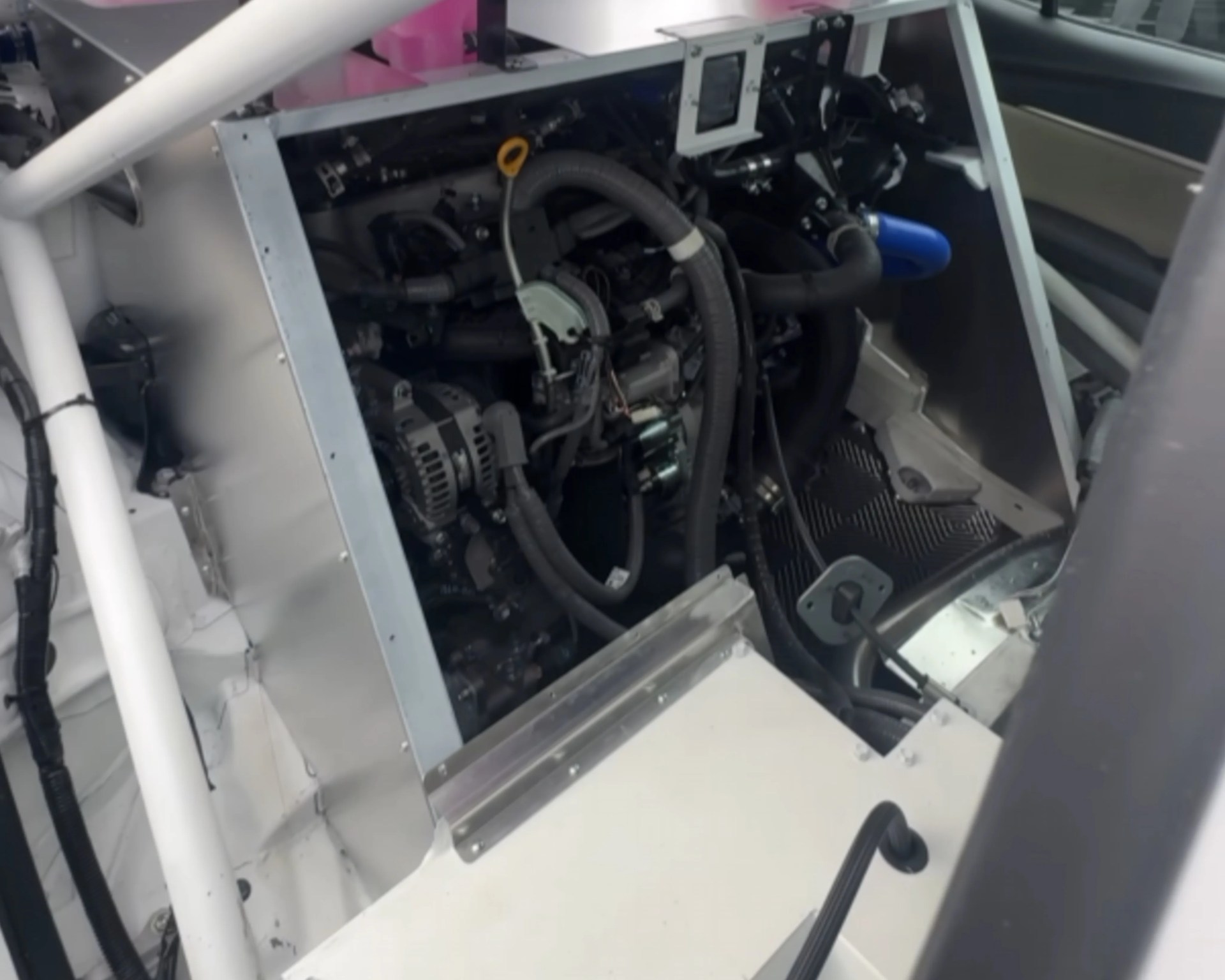 Engine compartment with black hoses, metal frame, and white structural tubing inside a vehicle or machinery.