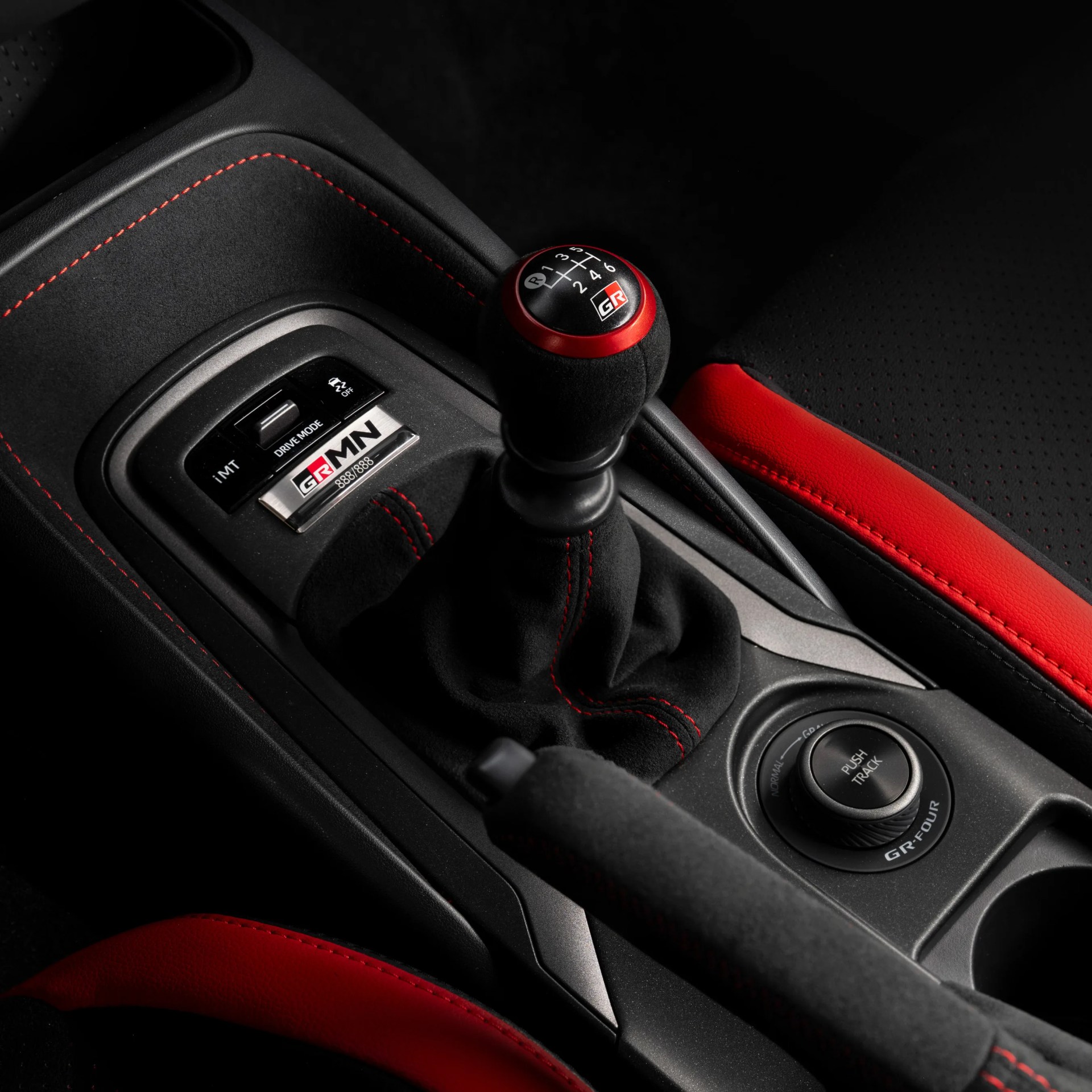 Black manual gear shift knob with red trim and GR logo, surrounded by black and red leather interior with red stitching.