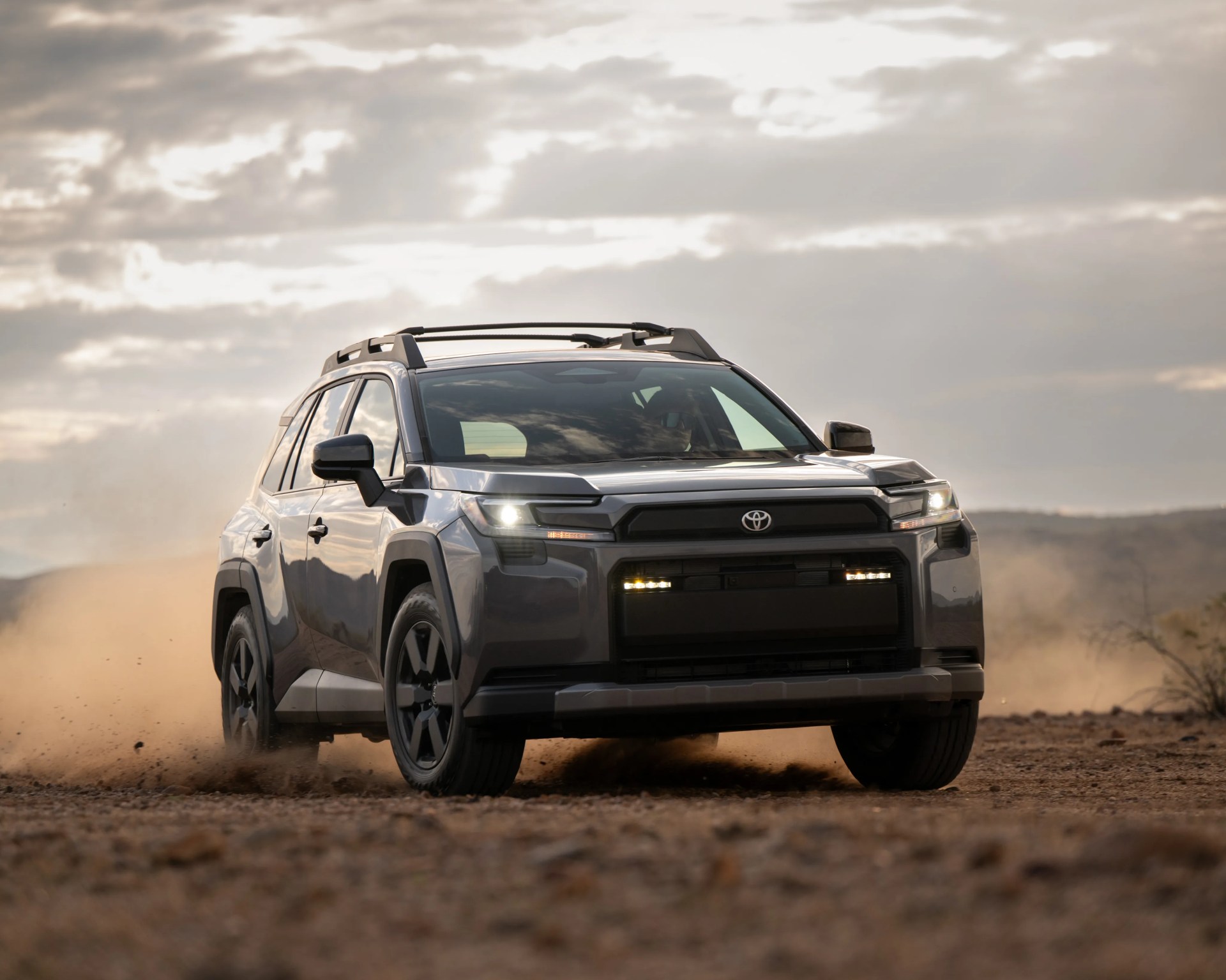 Gray Toyota SUV driving on a dusty dirt road under a cloudy sky.