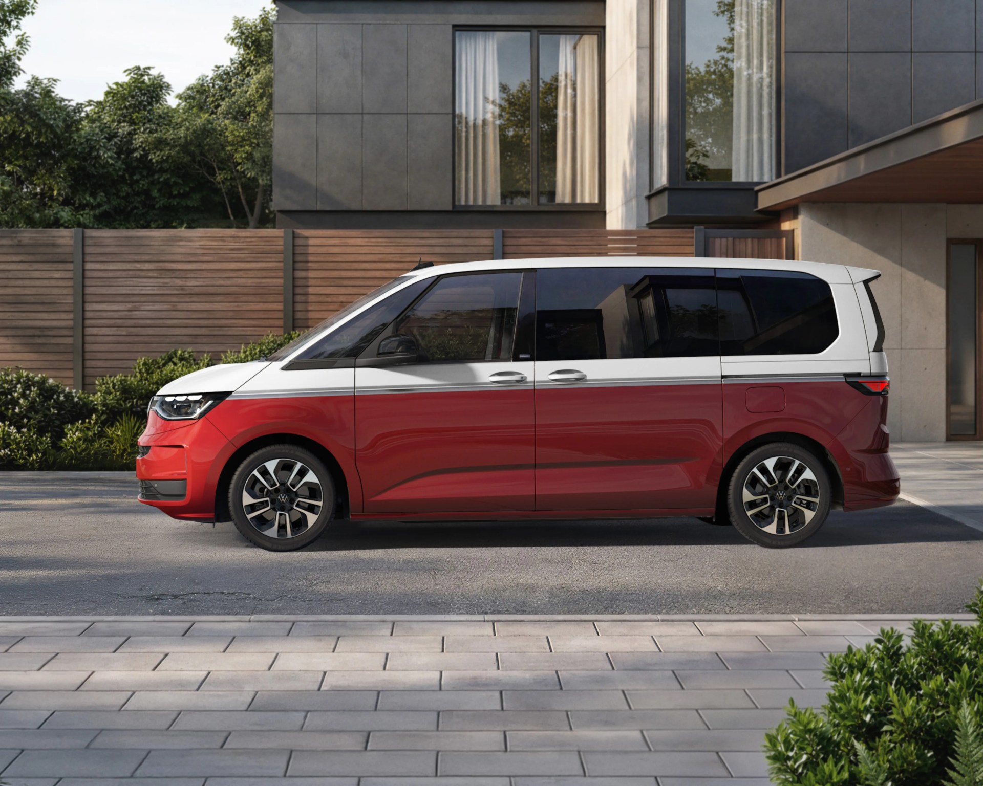 Red and white Volkswagen minivan parked on a street in front of a modern house with large windows.