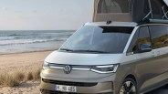 Silver Volkswagen camper van with pop-up roof parked on a sandy beach near the ocean.