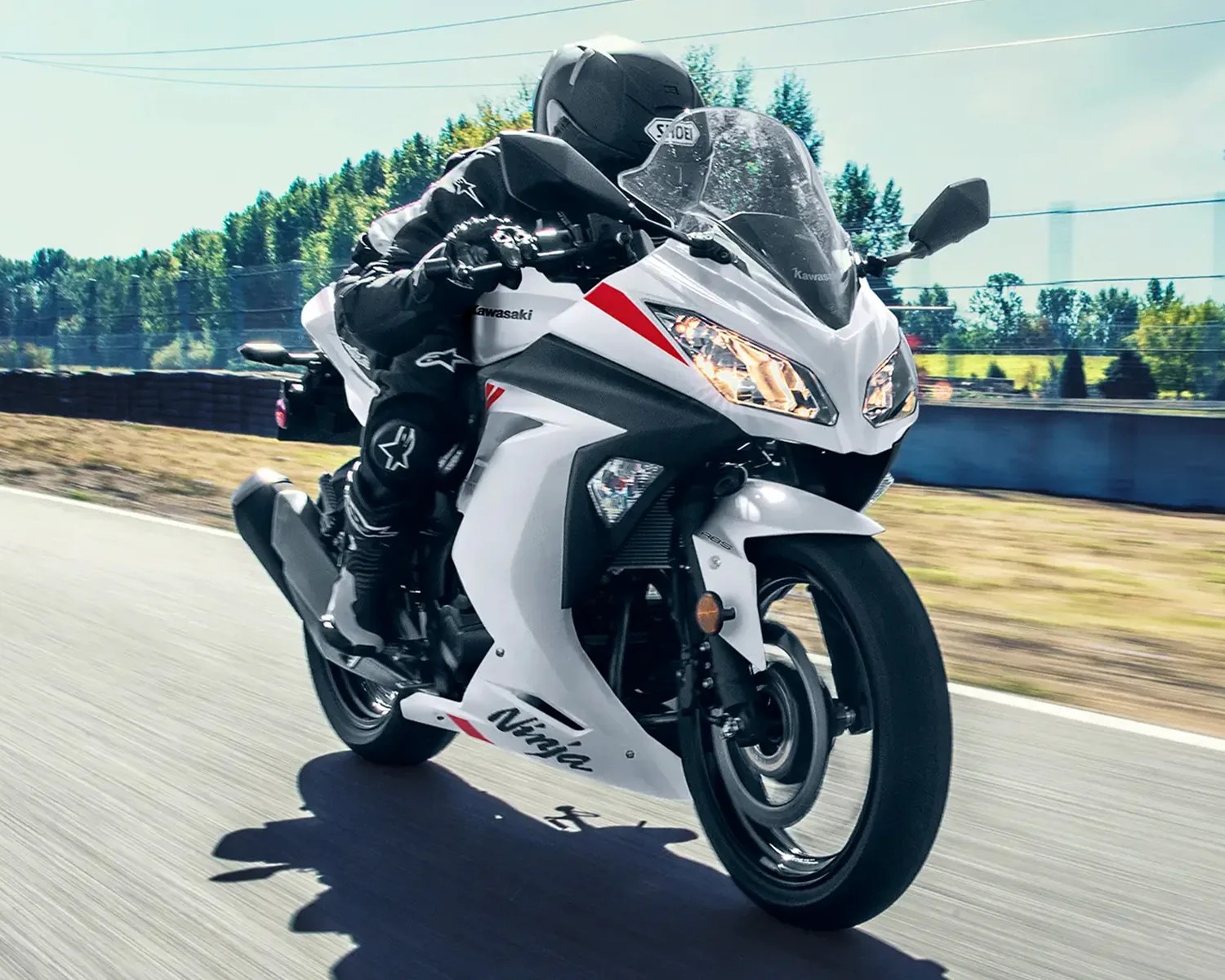 White Kawasaki Ninja sport motorcycle with red accents ridden on a paved road.