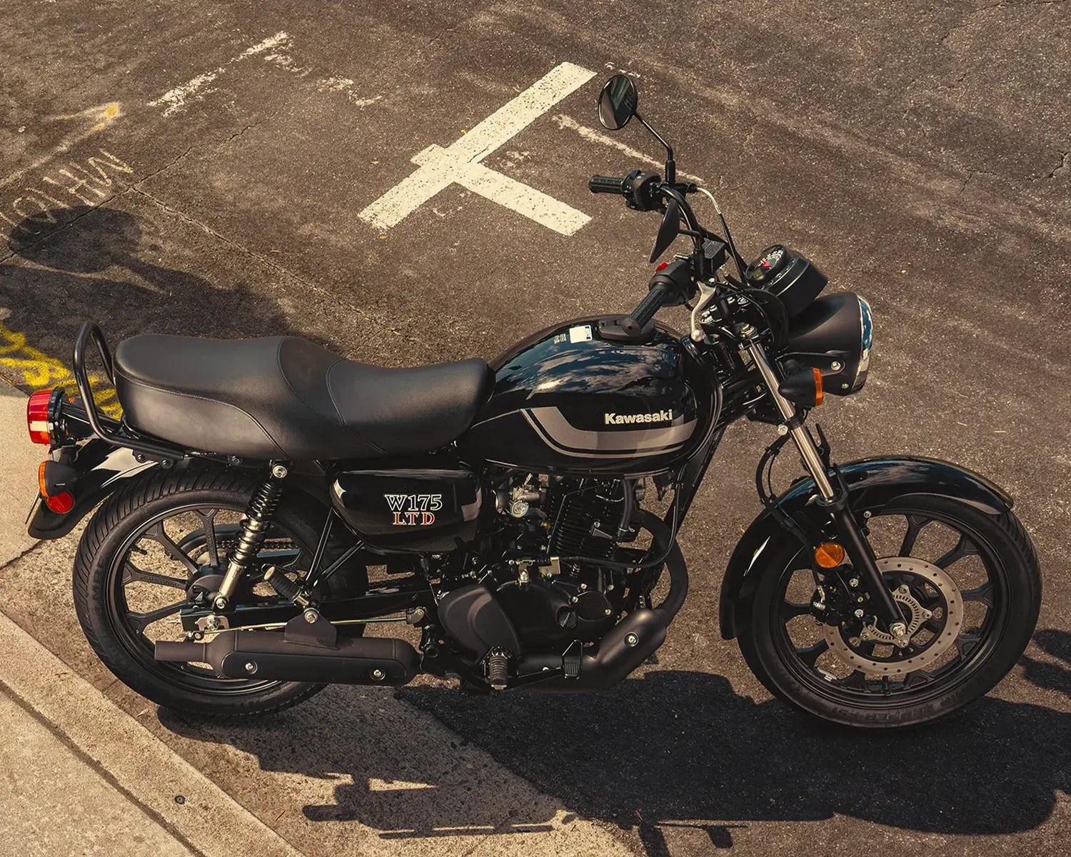 Black Kawasaki W175 LTD motorcycle parked on asphalt near a concrete curb.