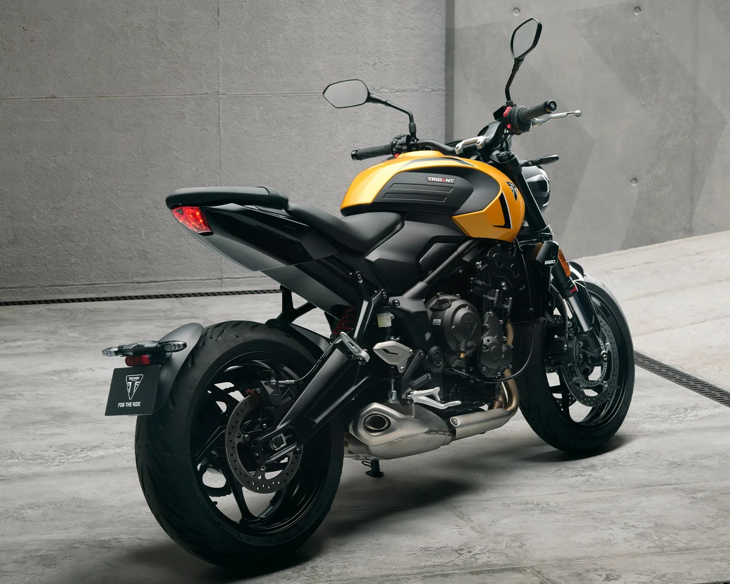 Yellow and black Triumph Trident 660 motorcycle parked on a concrete floor against a gray wall.