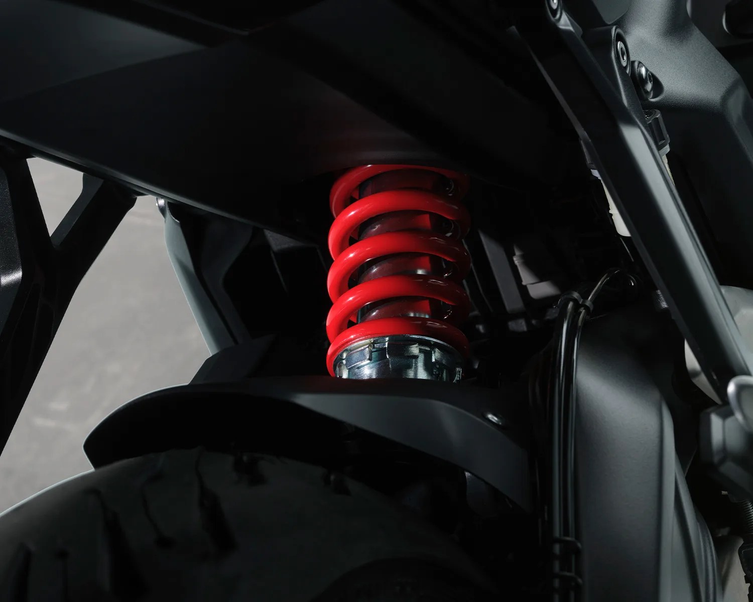 Close-up of a red coil spring suspension on a black motorcycle frame above the rear tire.