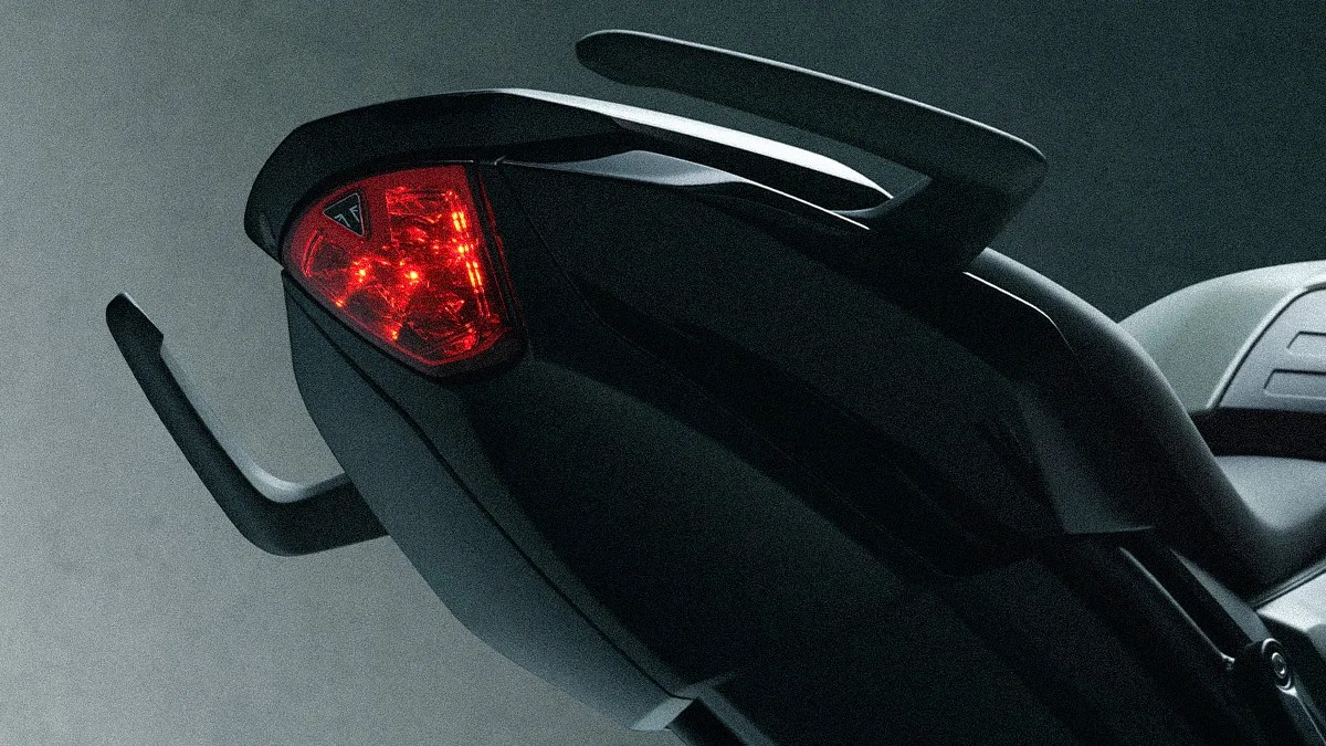 Rear section of a black motorcycle with illuminated red tail light and integrated rear grab handles.
