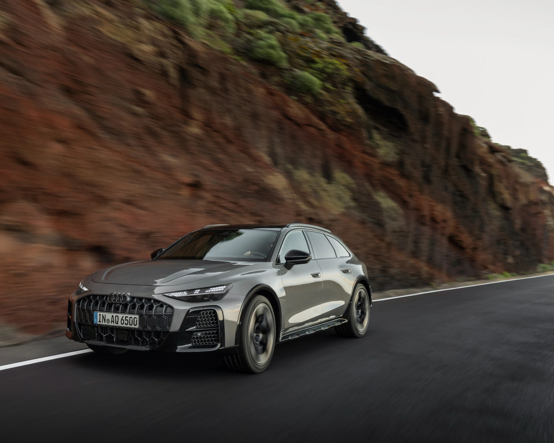 Gray Audi SUV driving on a road with rocky cliffs in the background.