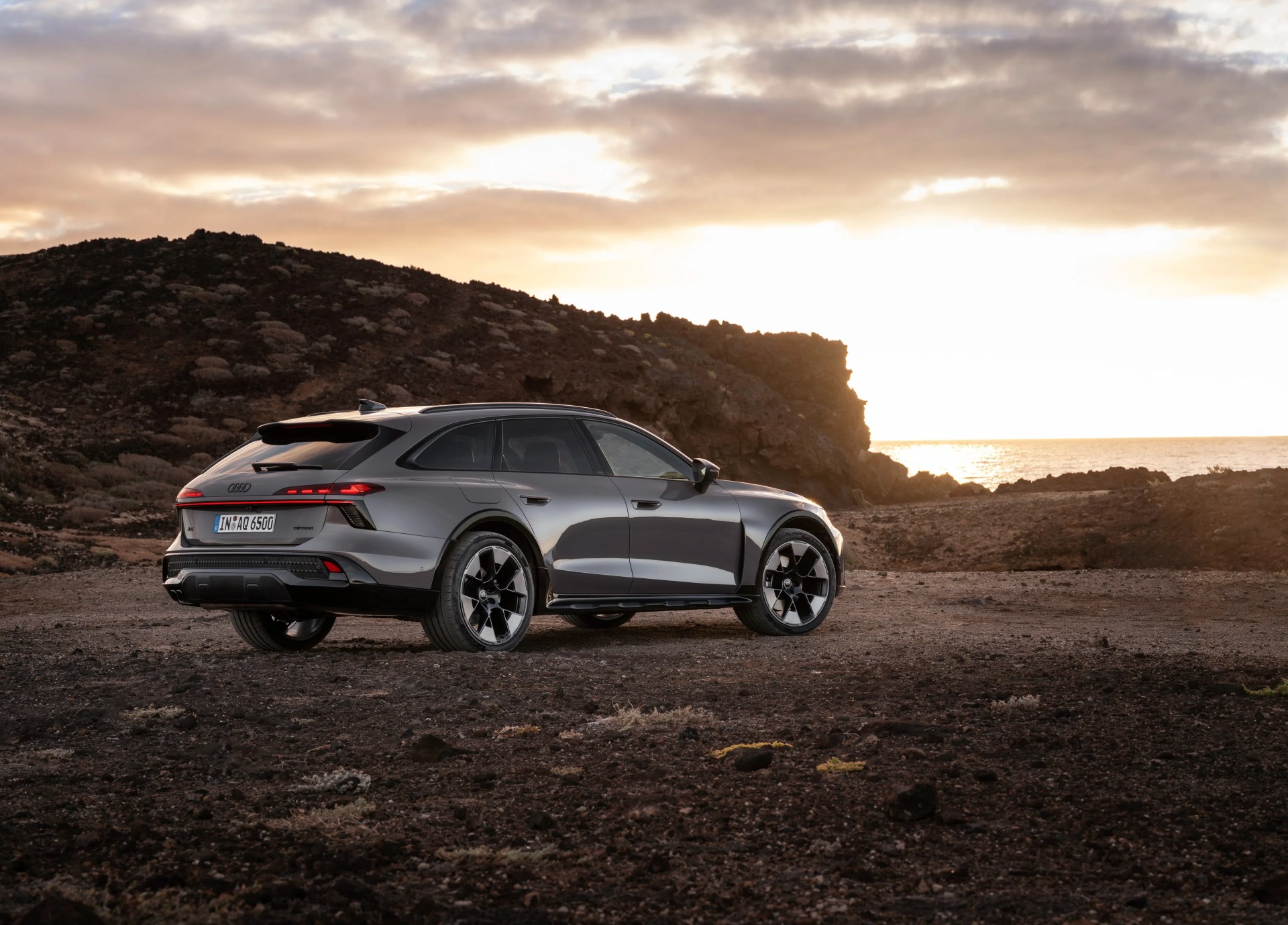 Gray Audi A6 Avant e-tron electric wagon parked on rocky terrain at sunset.