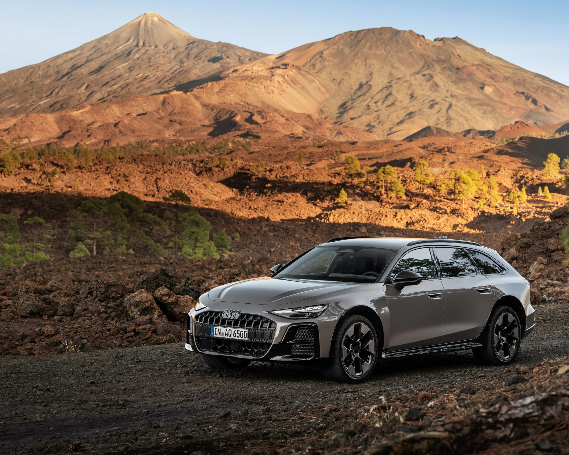 Gray Audi station wagon parked on rocky terrain with mountains in the background.