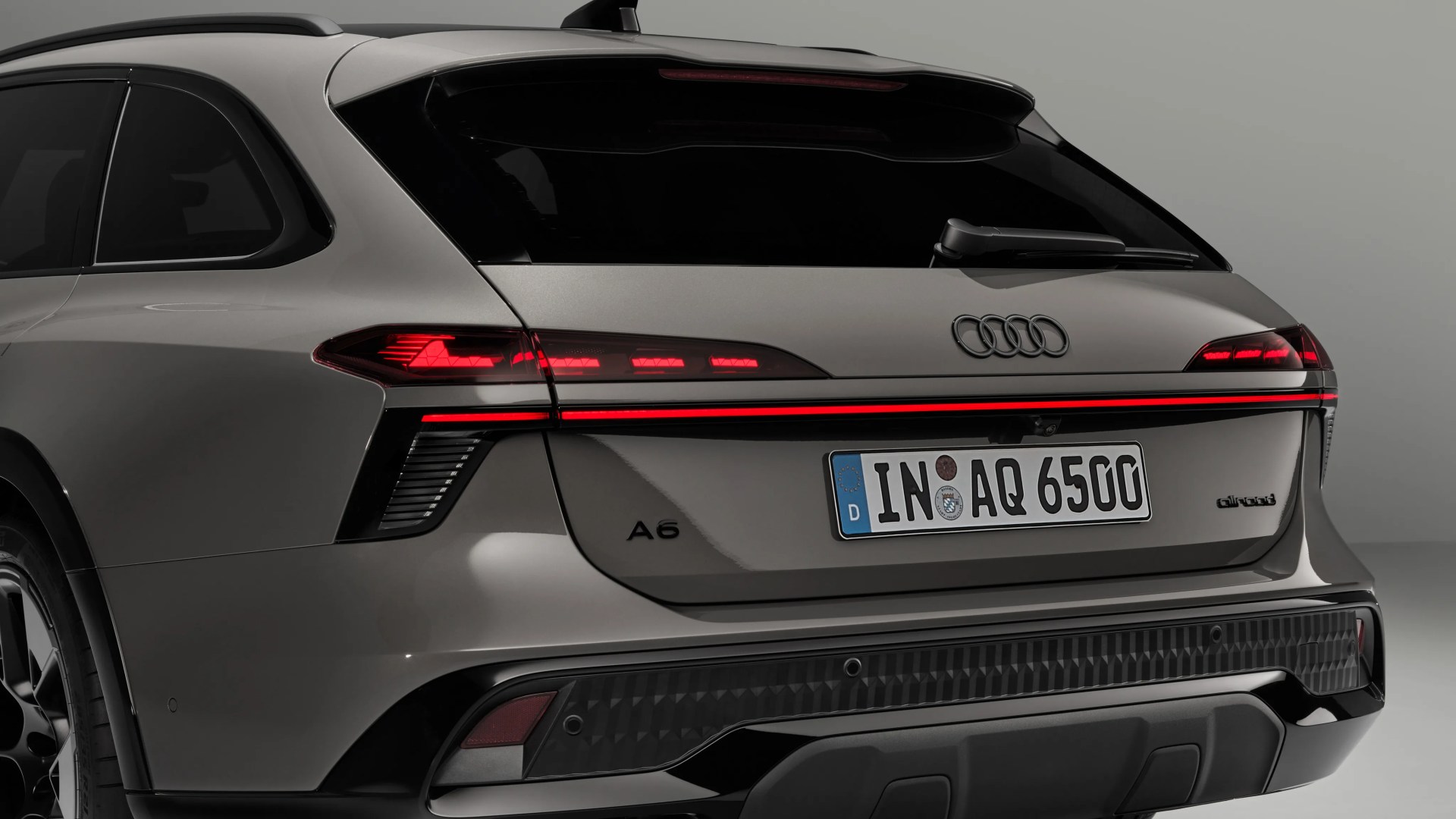 Rear view of a gray Audi A6 allroad with illuminated taillights and a European license plate.