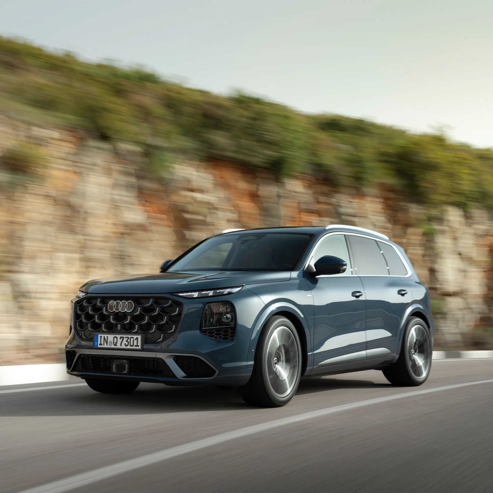 Blue Audi SUV driving on a road with a rocky hillside in the background.