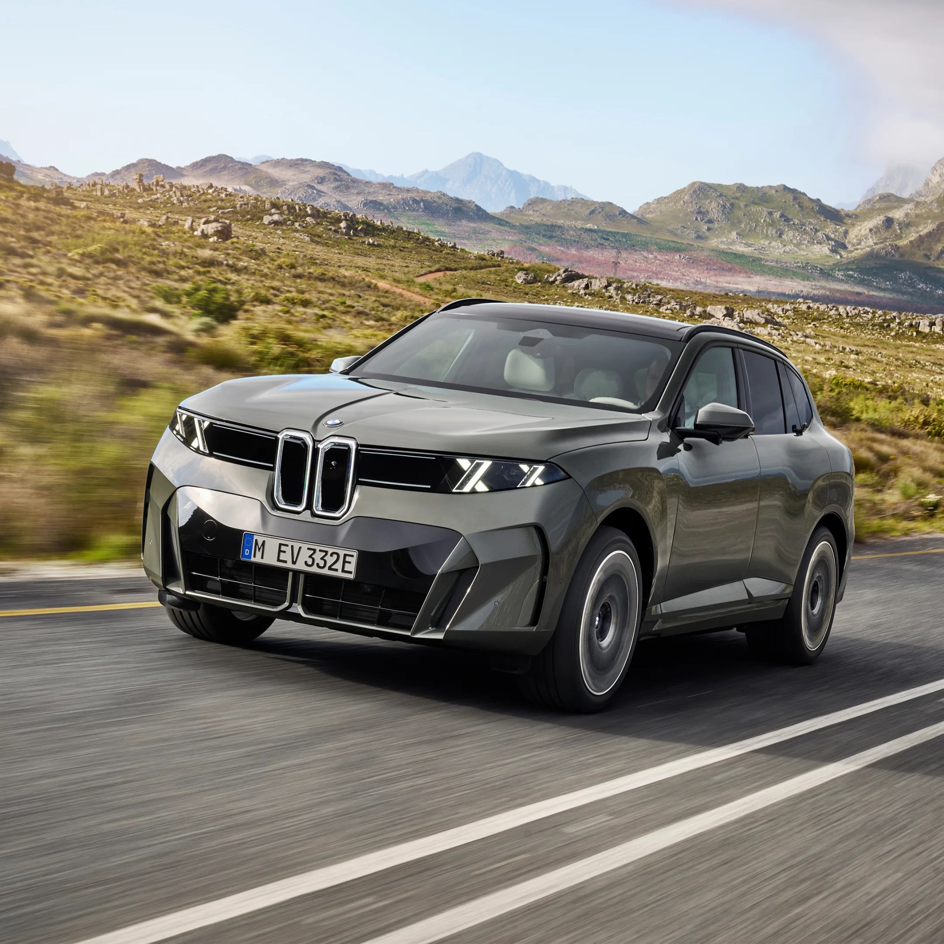 Gray BMW SUV driving on a mountain road with rocky hills in the background.