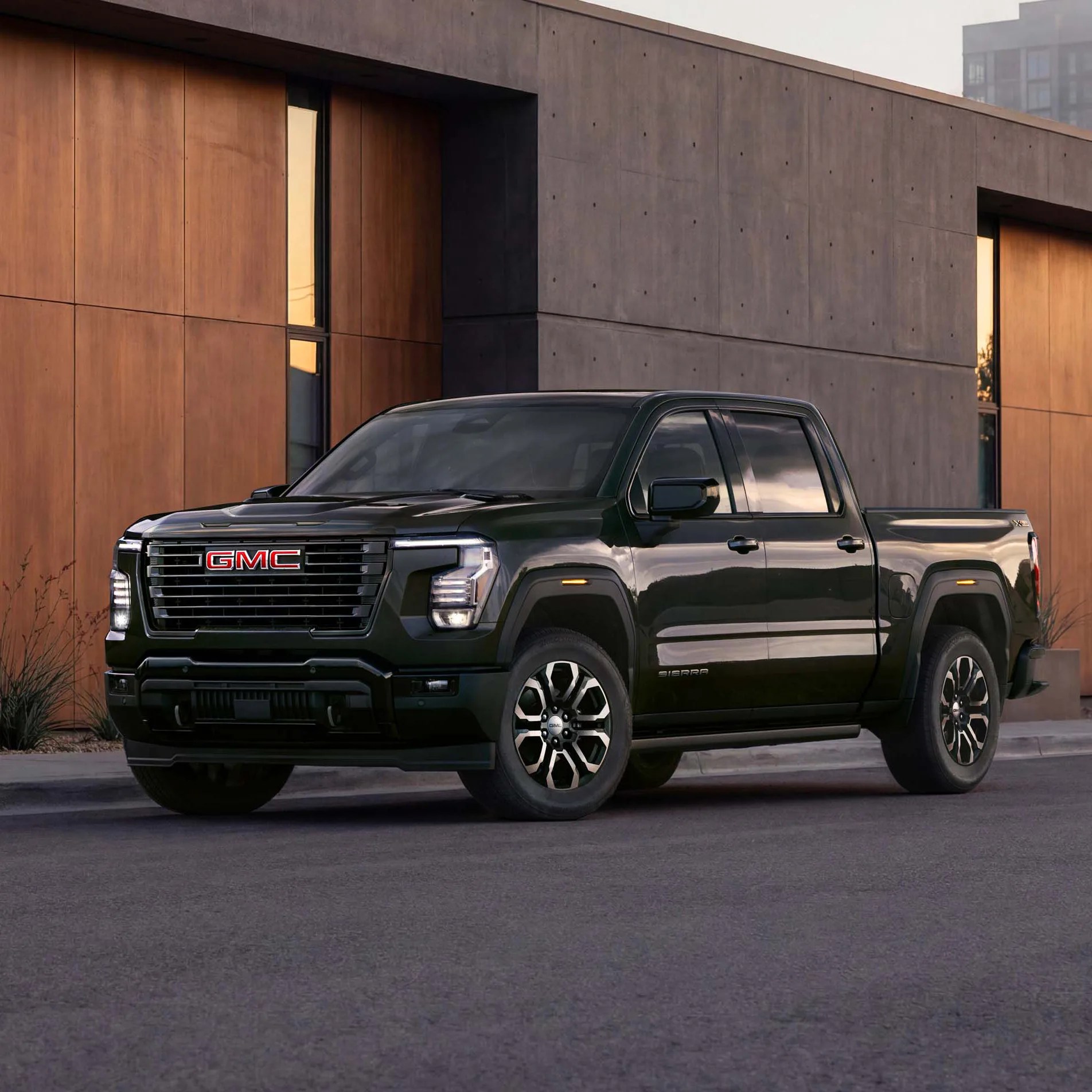 Black GMC Sierra pickup truck parked in front of a modern building with wood and concrete panels.