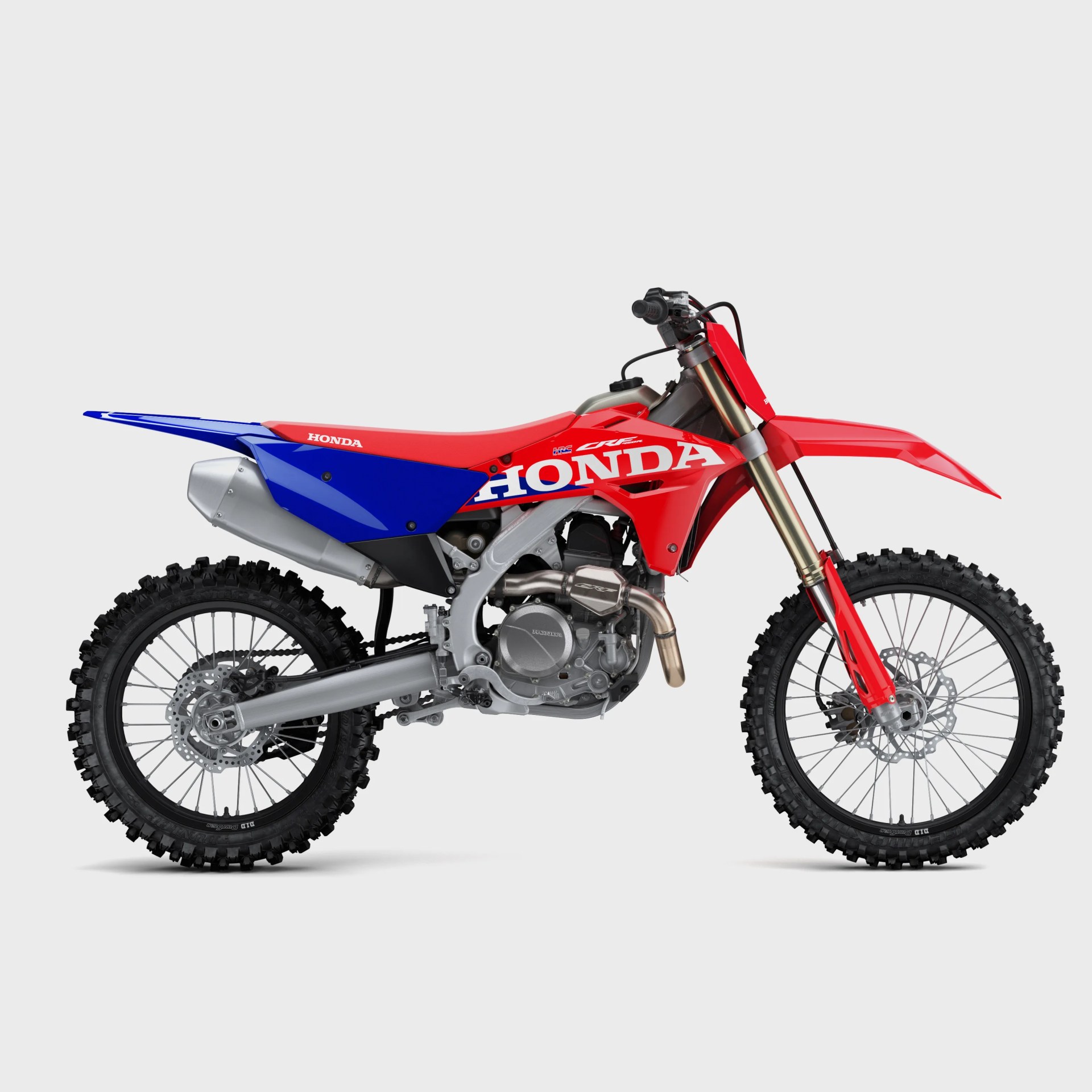Red and blue Honda CRF dirt bike with knobby tires and silver exhaust on a gray background.