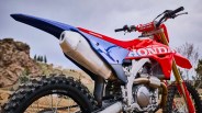 Red and blue Honda dirt bike with knobby tires and Renthal handlebars in an outdoor setting.