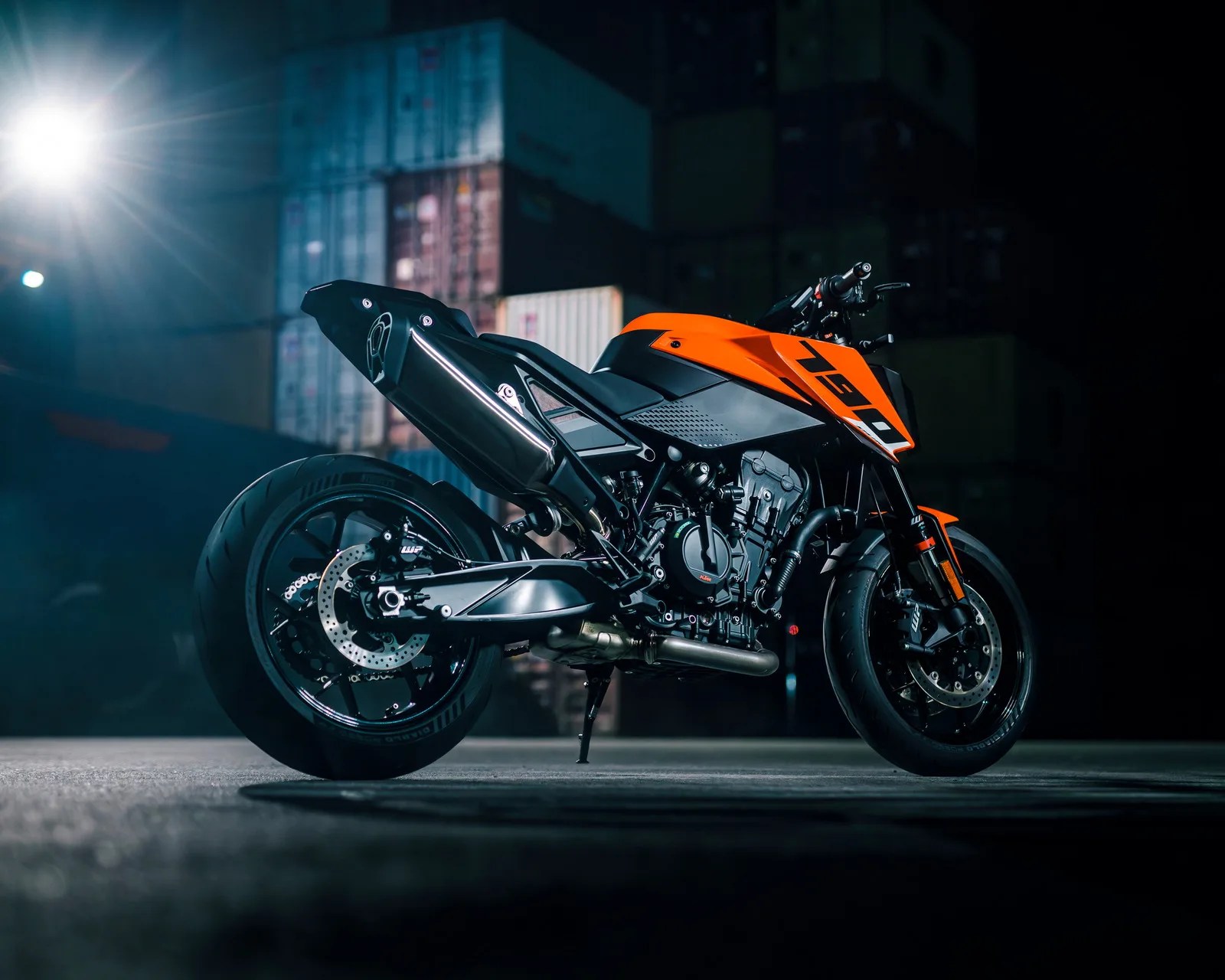 Orange and black KTM 790 motorcycle parked on a concrete surface with shipping containers in the background at night.