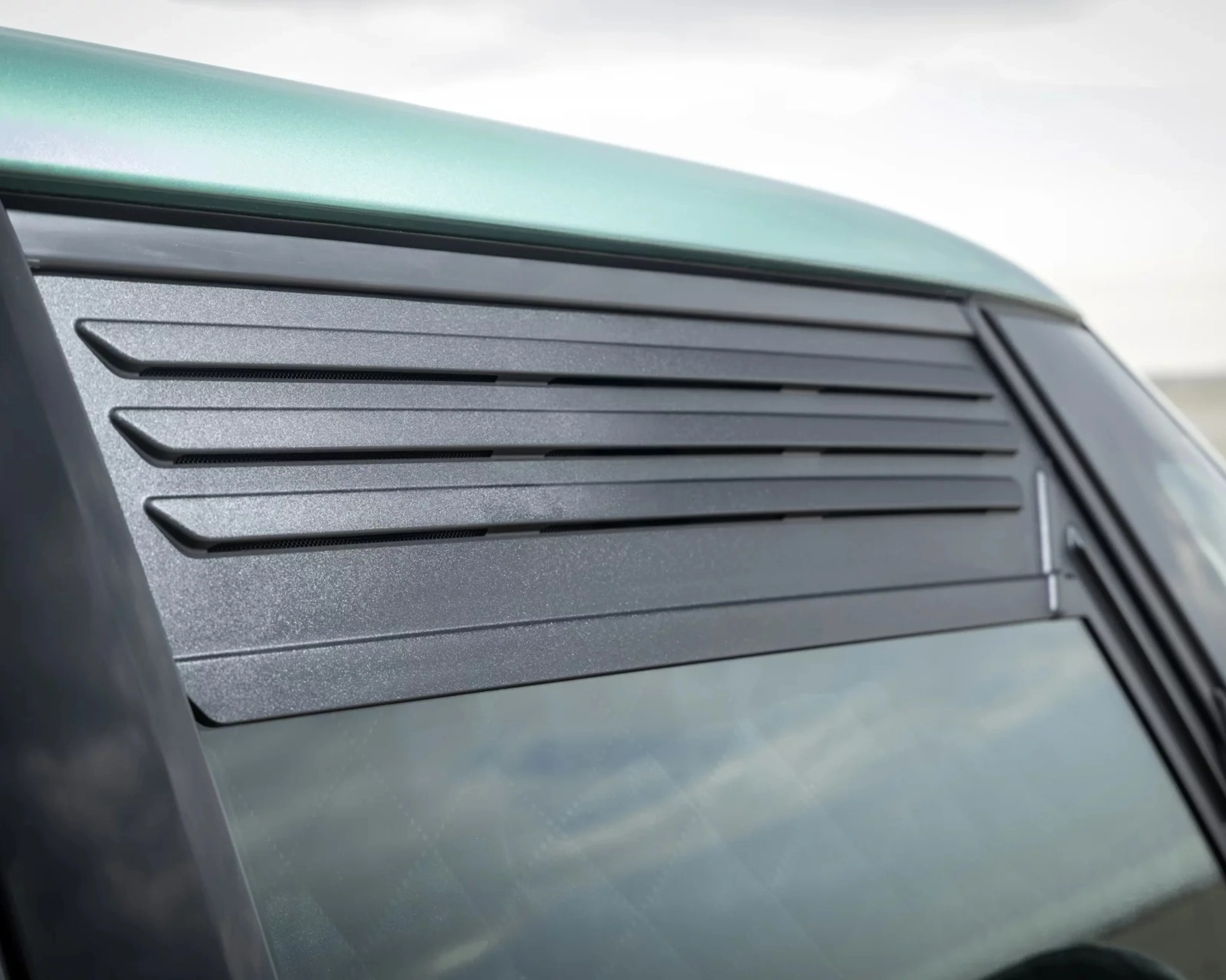 Close-up of a black rear window louver on a green vehicle.