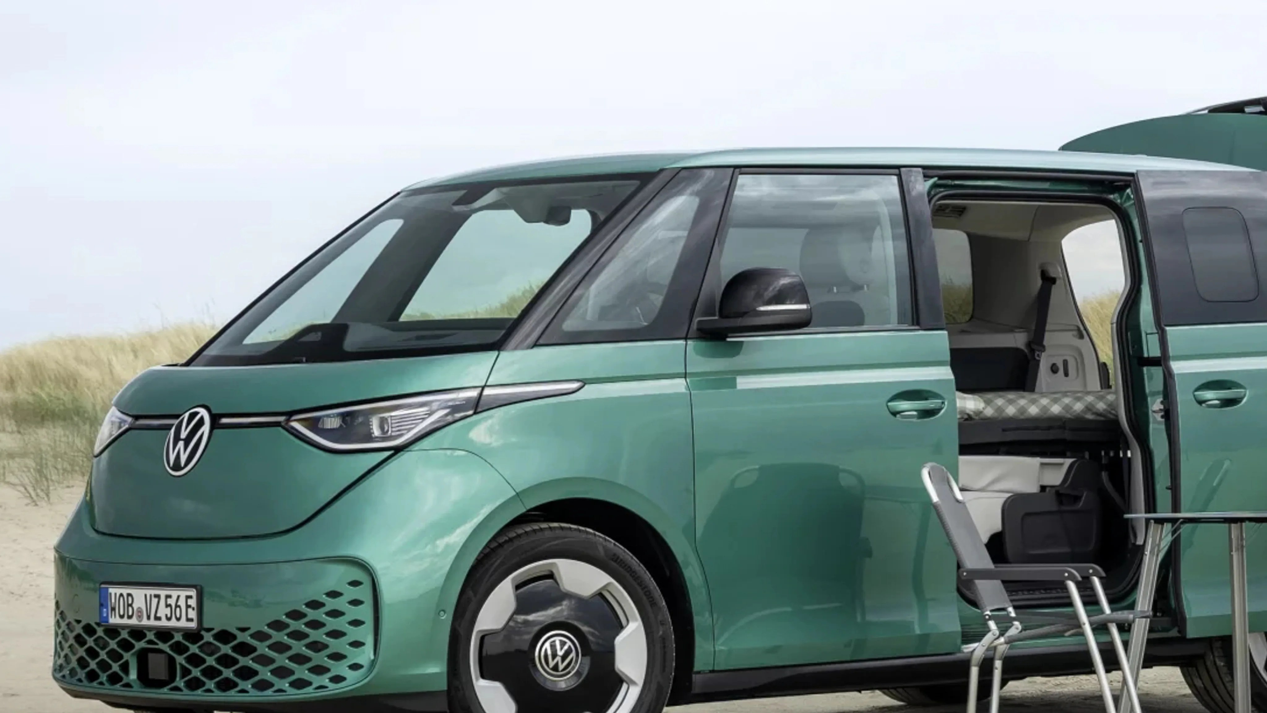 Green Volkswagen electric van with sliding door open and camping chair and table outside.