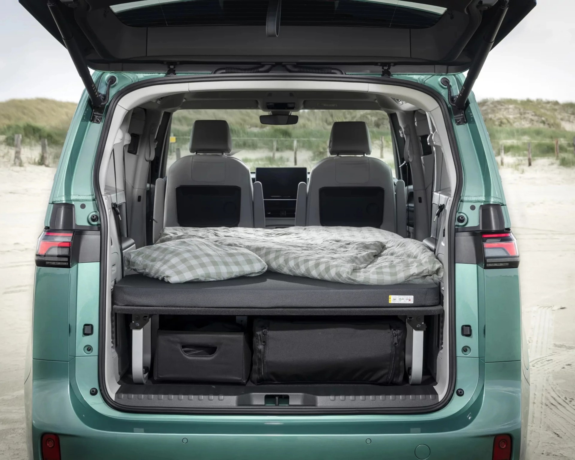 Open rear of a teal van showing a folded bed with checkered bedding and storage compartments underneath.