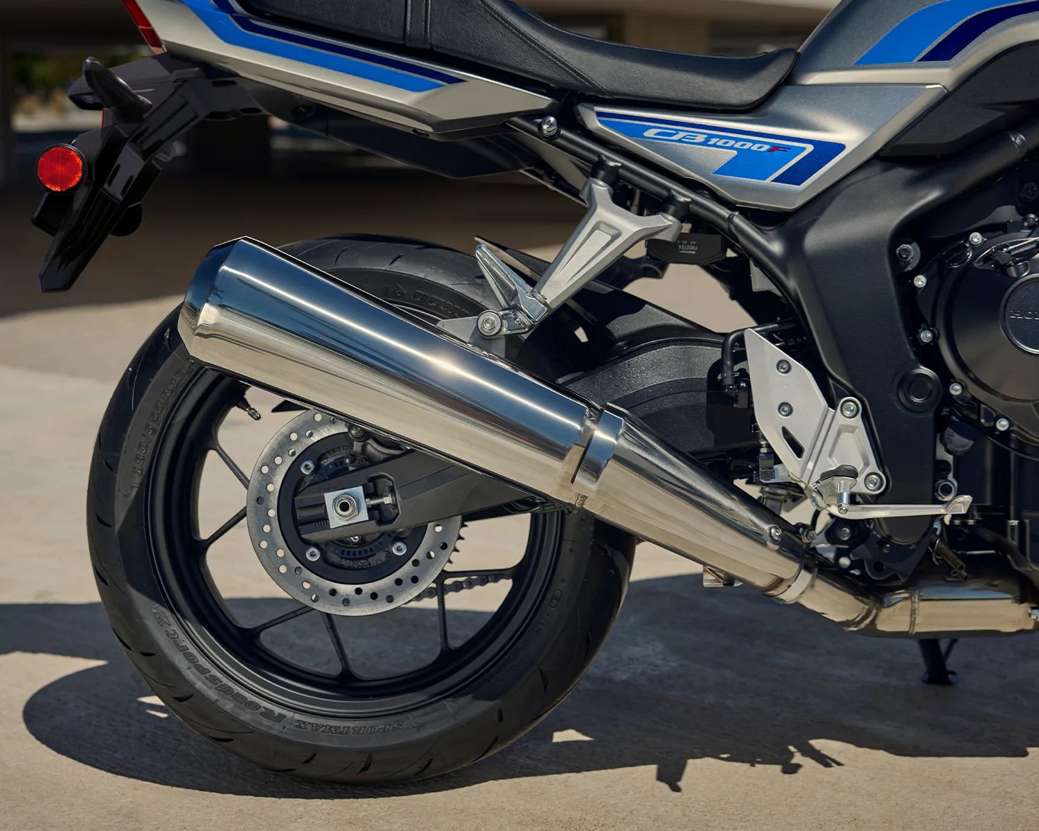 Rear section of a blue and silver CB1000F motorcycle showing the rear wheel, exhaust pipe, and part of the seat.