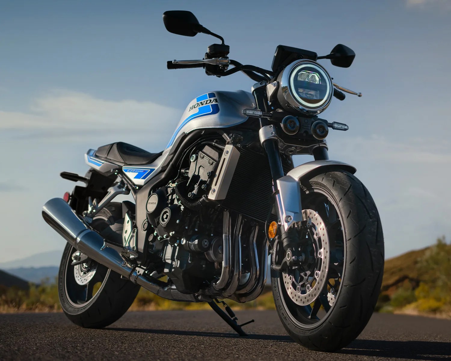 Silver and blue Honda motorcycle with round headlight parked on road with clear sky background.