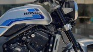 Close-up of a silver Honda motorcycle fuel tank with blue stripes and part of the black engine and front fork.