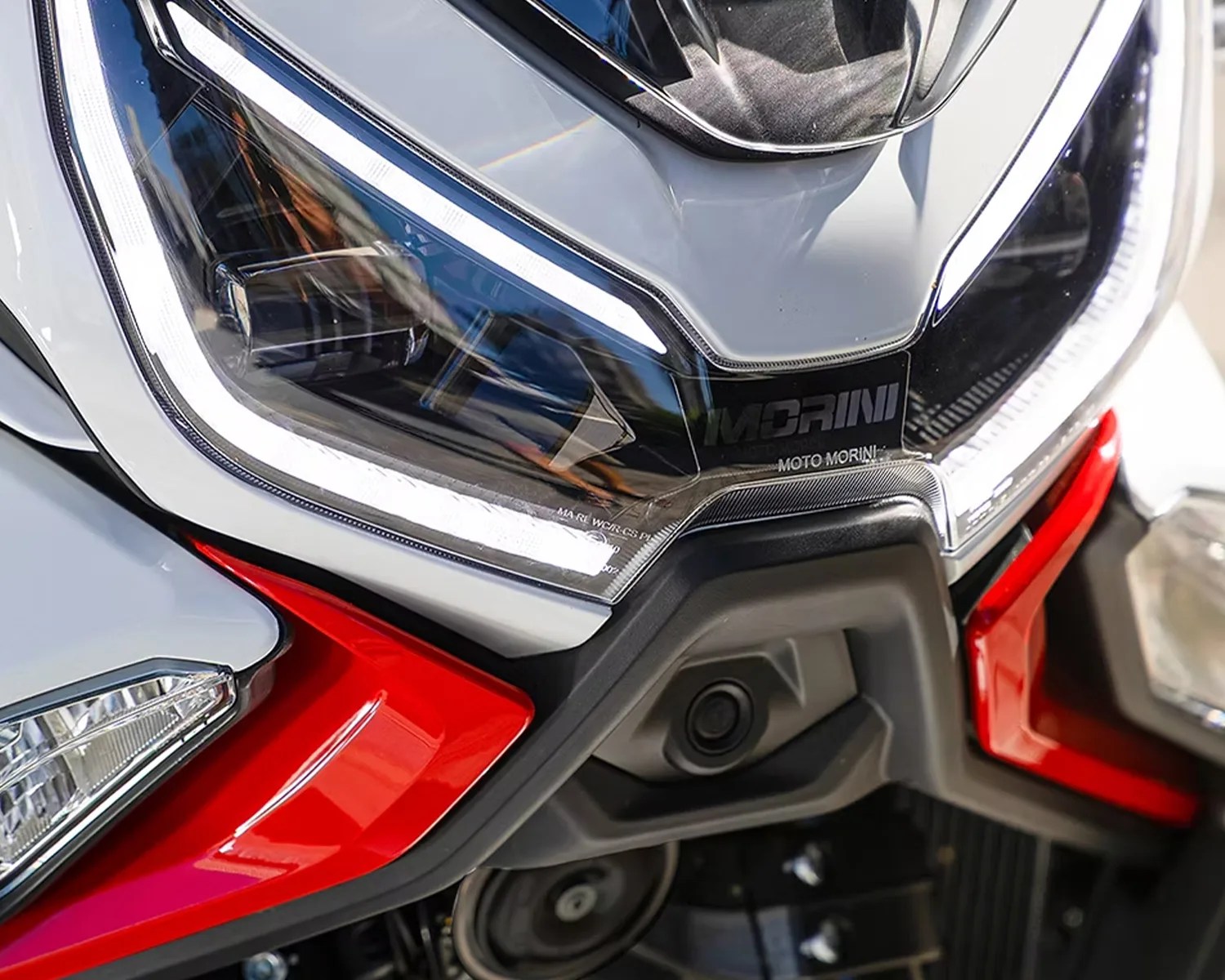 Close-up of a motorcycle headlight with white LED accents, red and gray body panels, and "Moto Morini" branding.