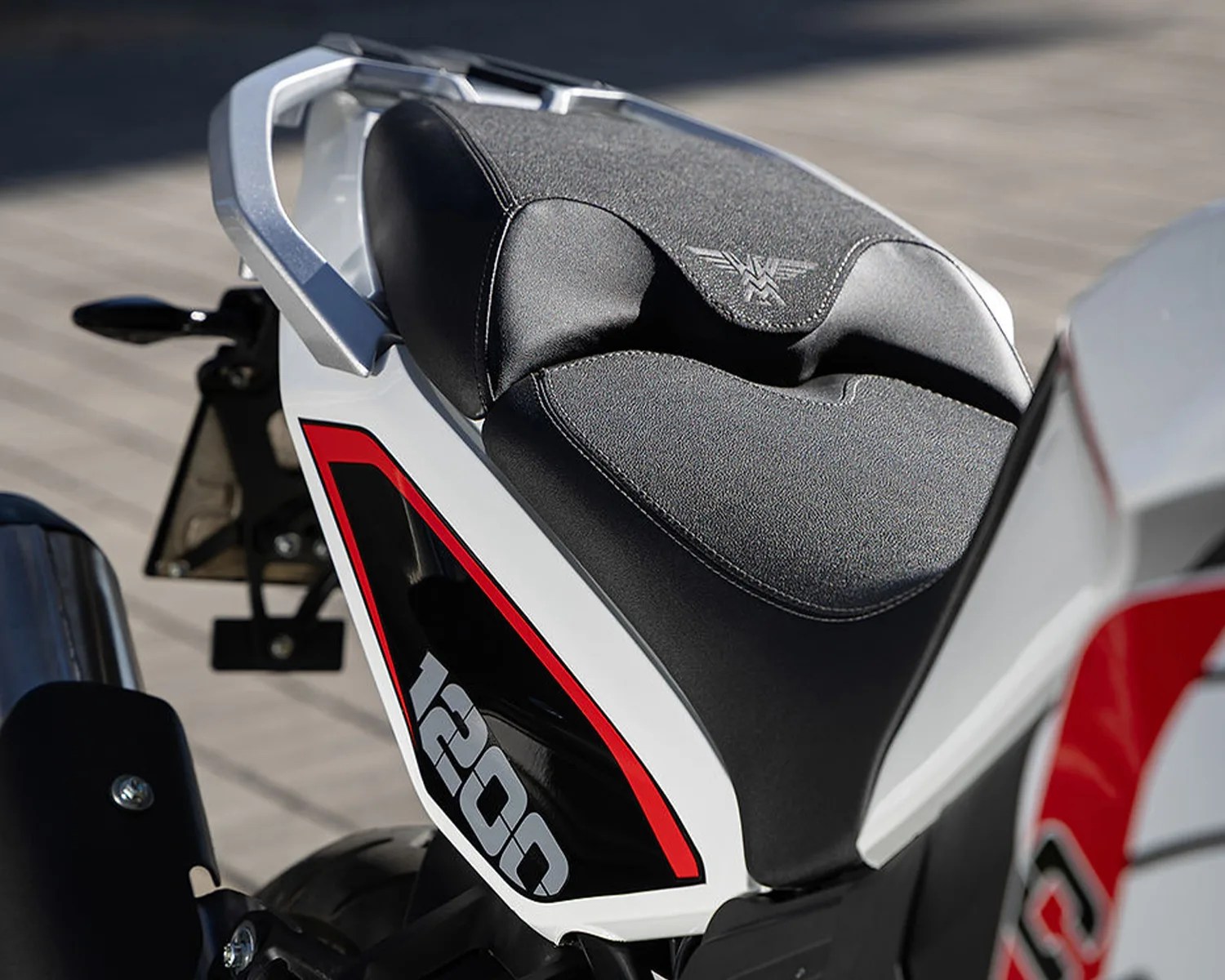 Black textured motorcycle seat with a silver emblem on a white bike frame labeled "1200" with red and black accents.