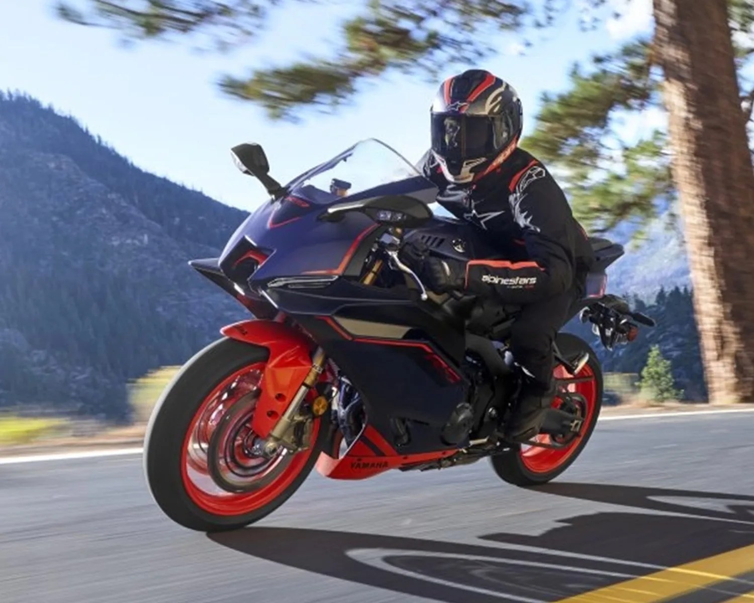 Sport motorcycle with black and red body and red wheels ridden on a mountain road.
