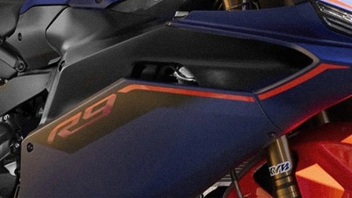 Close-up of a blue motorcycle fairing with red "RS" lettering and gold front suspension forks.