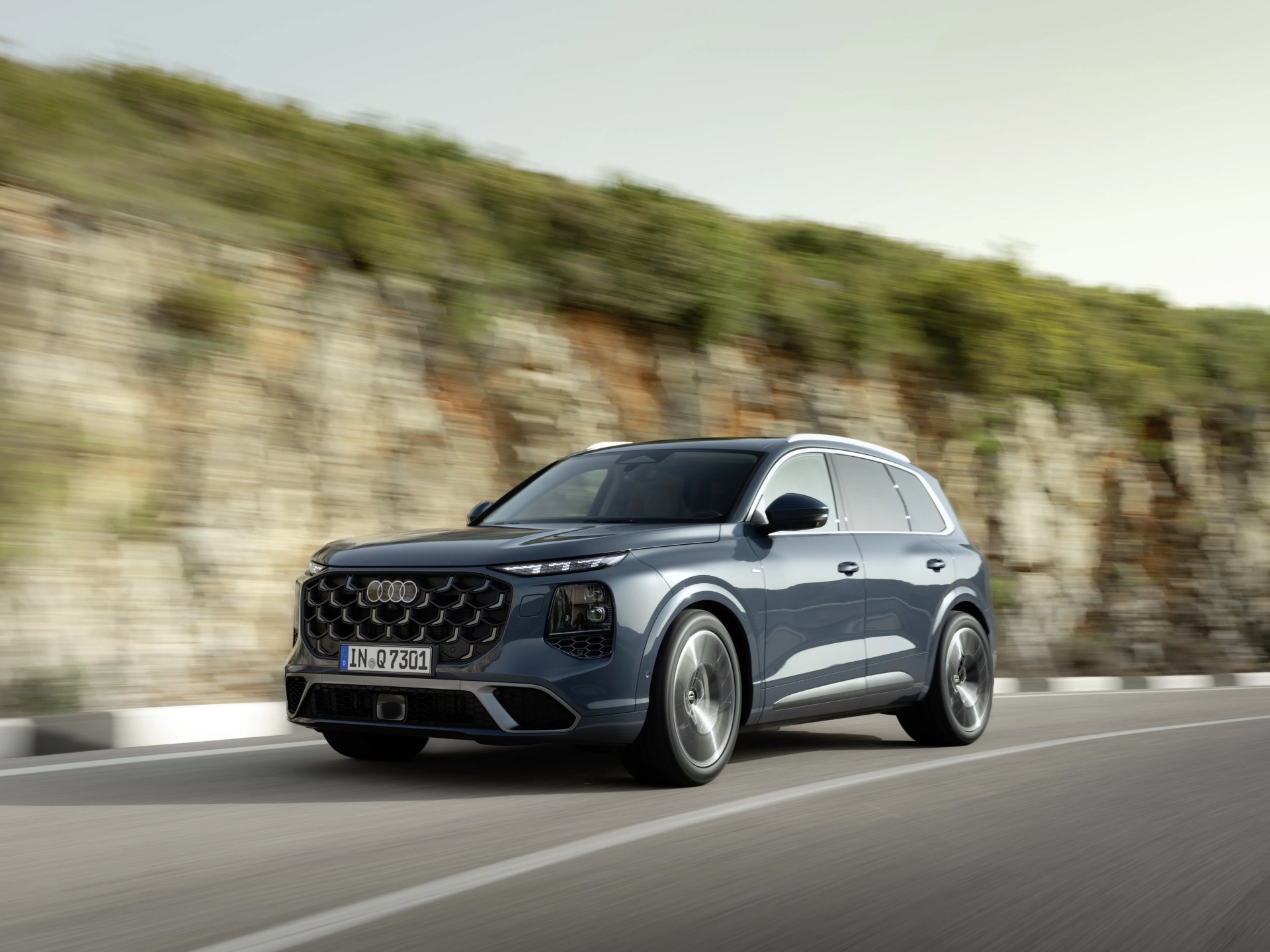 Dark gray Audi SUV driving on a road with a rocky hillside in the background.