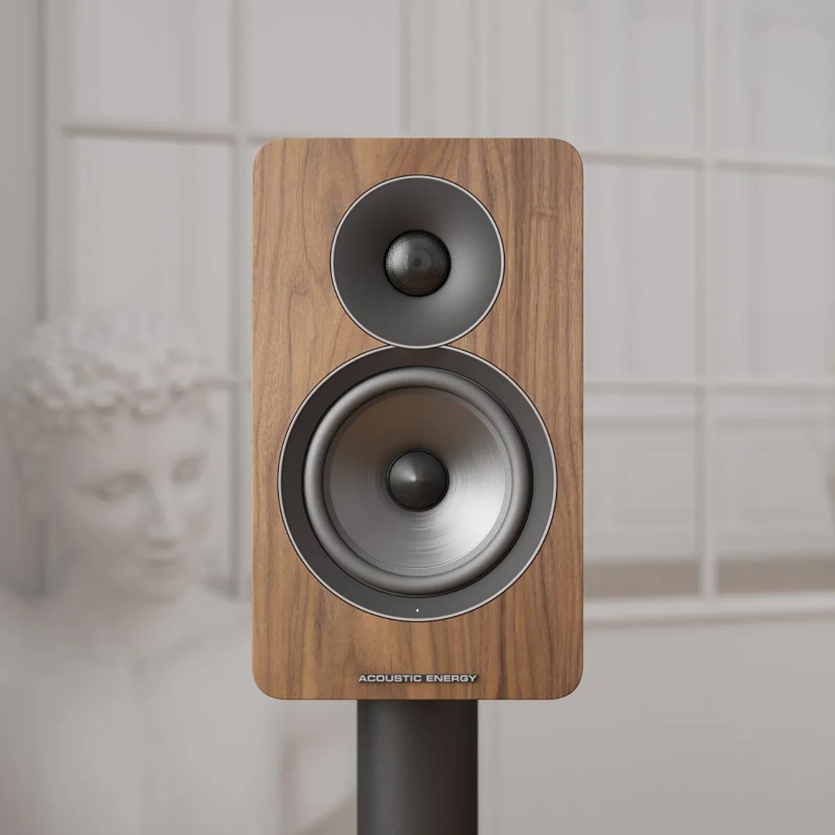 Wood-finished Acoustic Energy speaker with two drivers on a black stand in front of a window.
