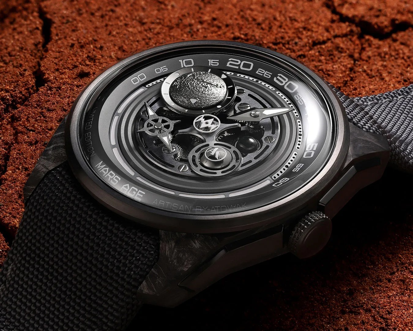 Black textured strap wristwatch with a complex mechanical dial labeled "Mars Age" on a reddish soil background.