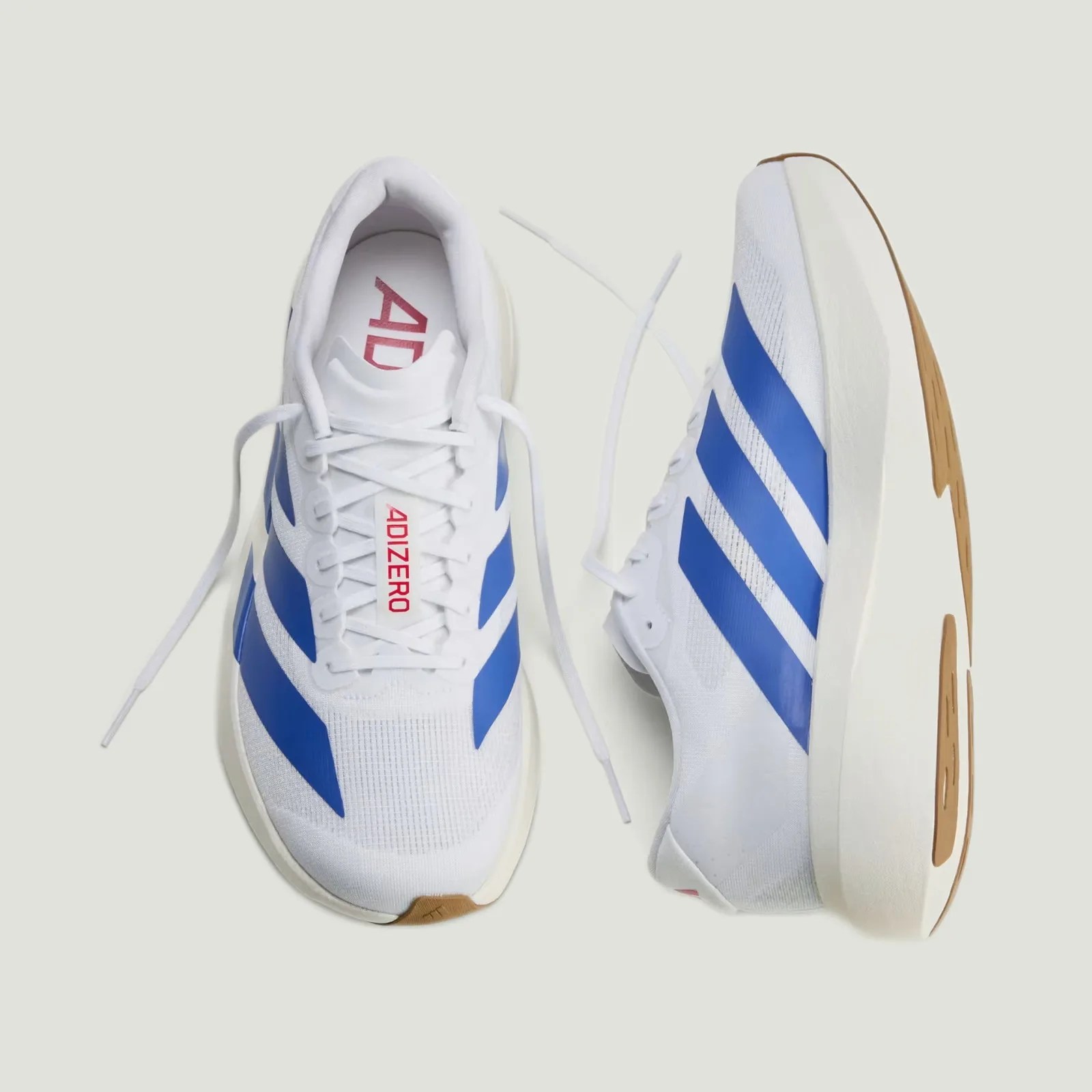 Pair of white Adidas Adizero running shoes with blue stripes and gum-colored soles on a light background.