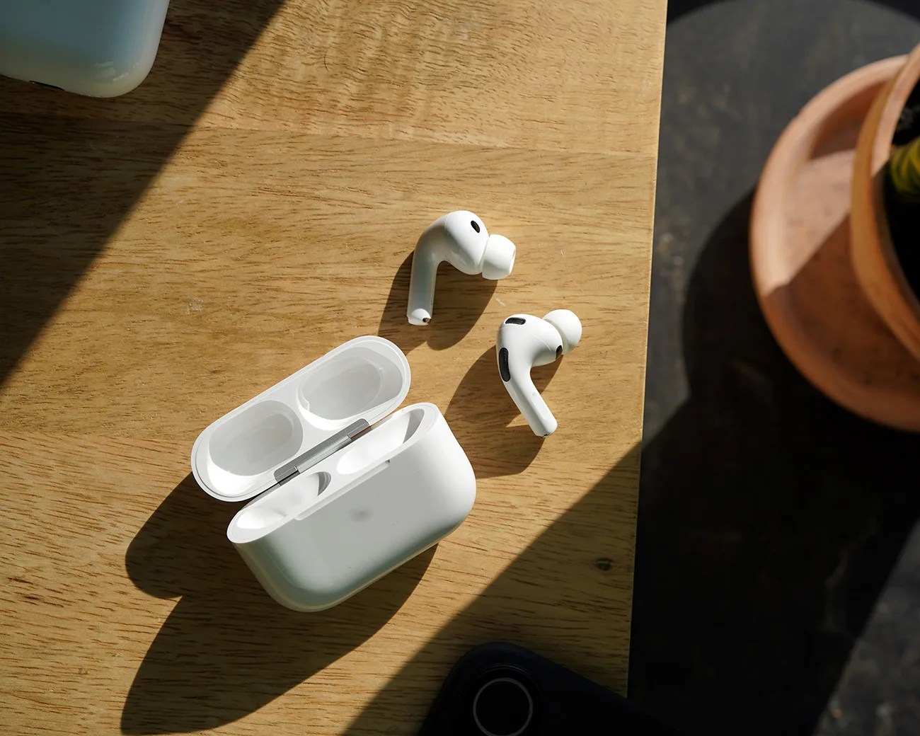 White wireless earbuds with silicone tips next to an open charging case on a wooden surface.