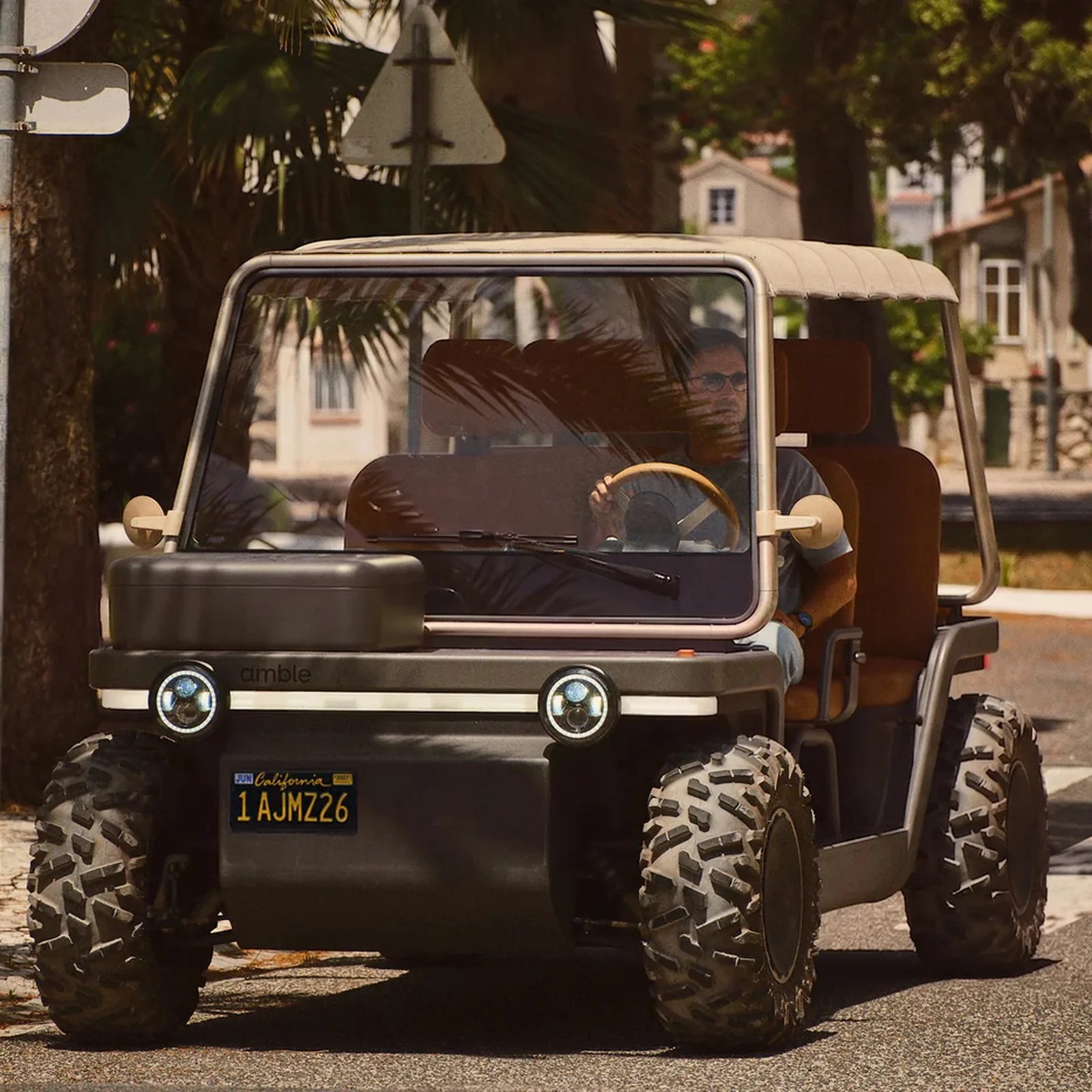 Compact off-road vehicle with large knobby tires, beige canopy, and brown seats driven on a street.