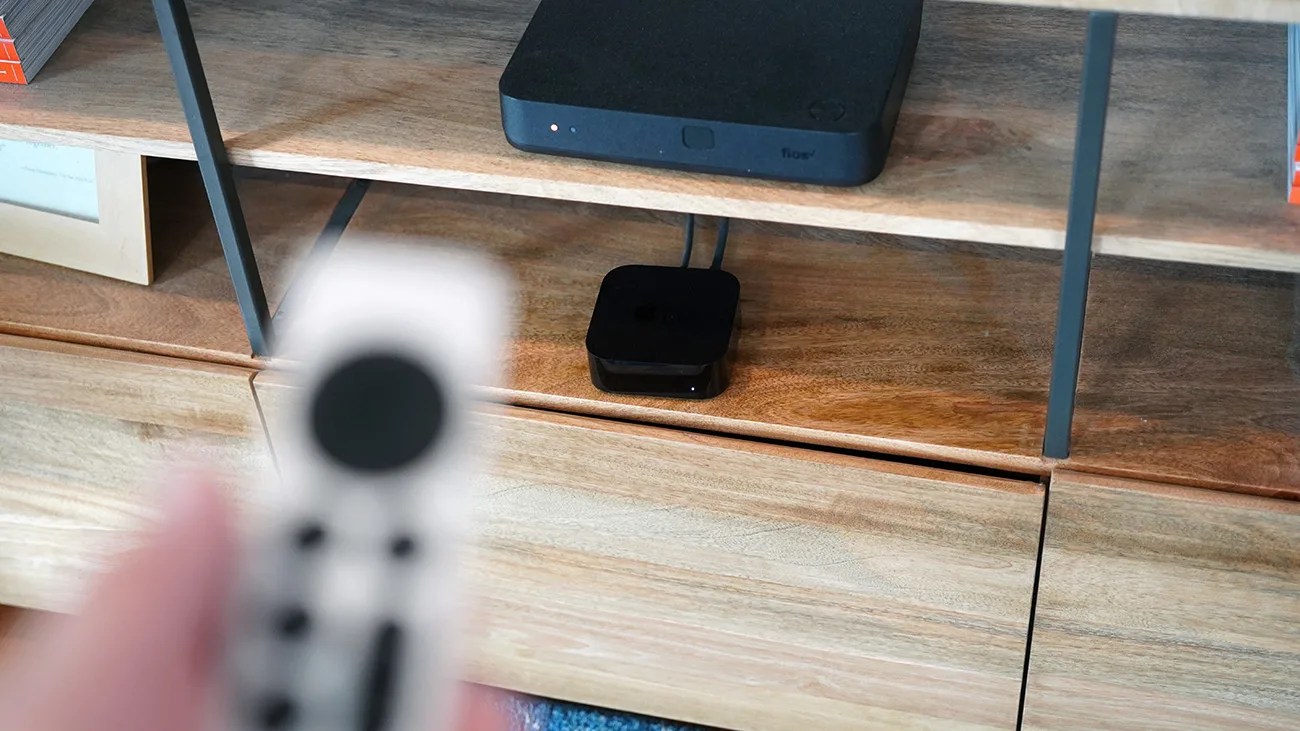 Black streaming device with cables on a wooden shelf below a black electronic device.