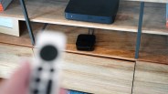 Black streaming device with cables on a wooden shelf below a black electronic device.
