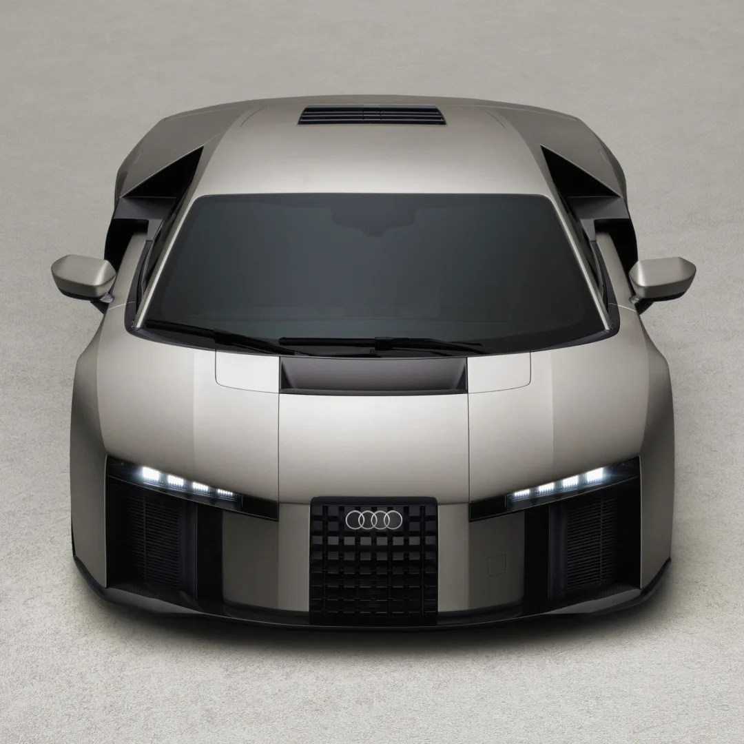 Front view of a silver Audi sports car with sleek angular design and LED headlights on a light gray surface.