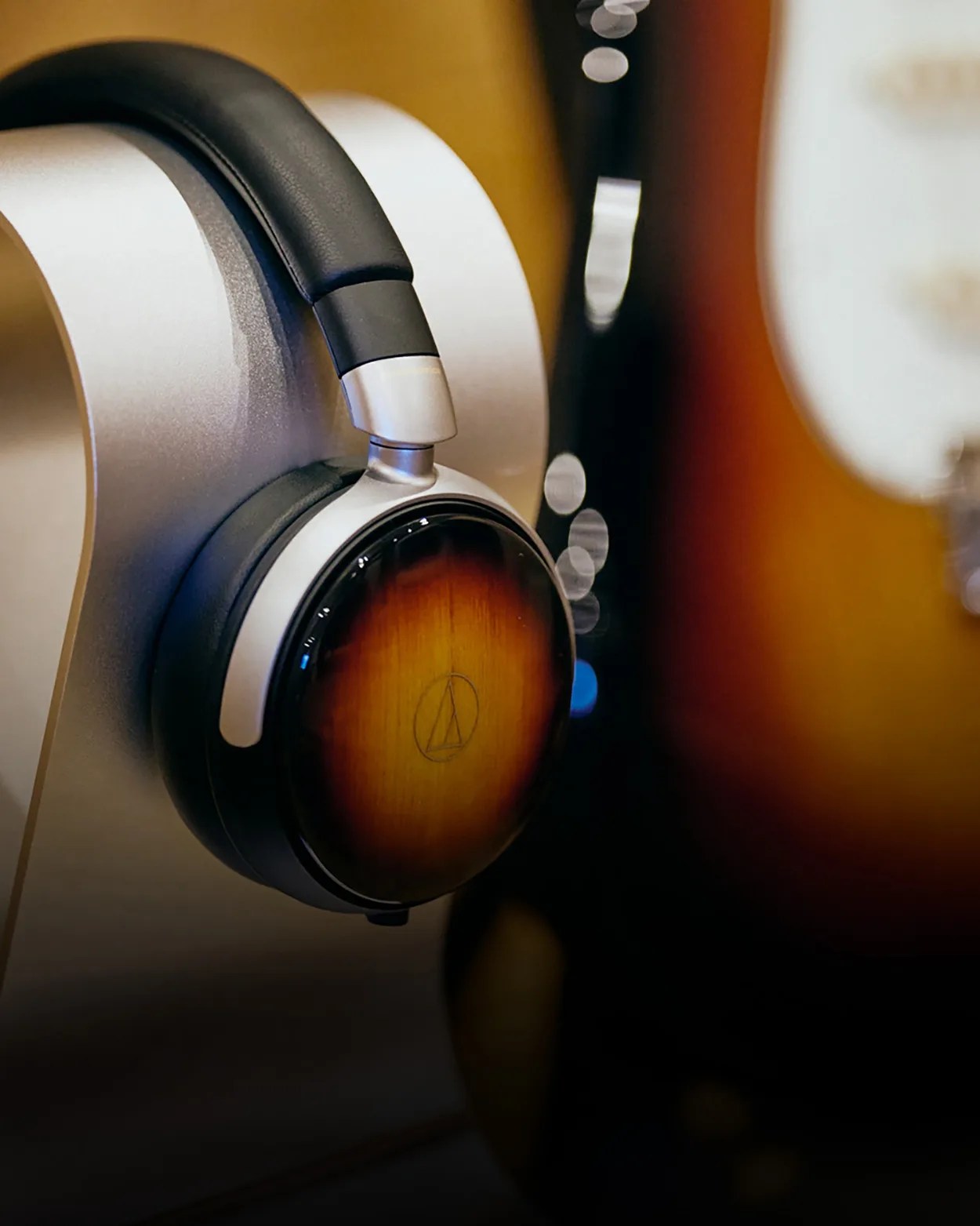 Over-ear headphones with wood-finish ear cups and black padded headband on a silver stand.