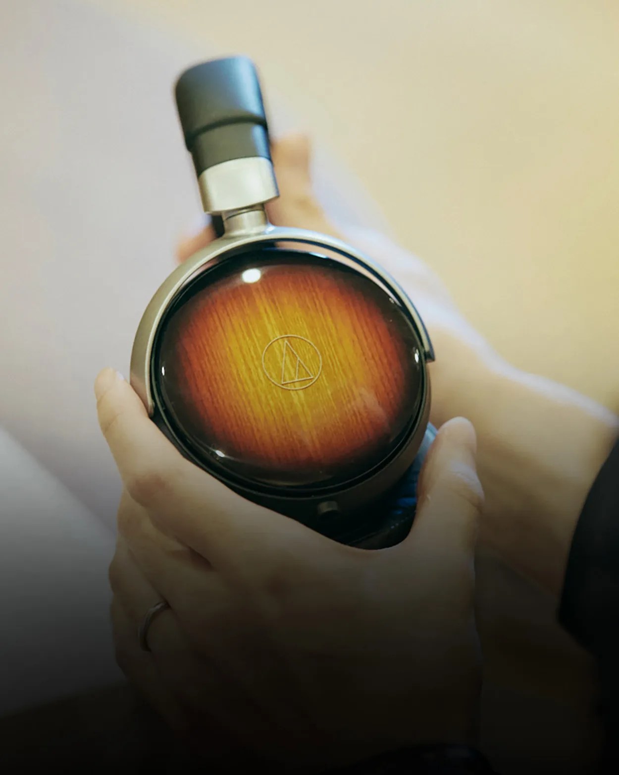 Hand holding a headphone earcup with a wood grain finish and Audio-Technica logo.