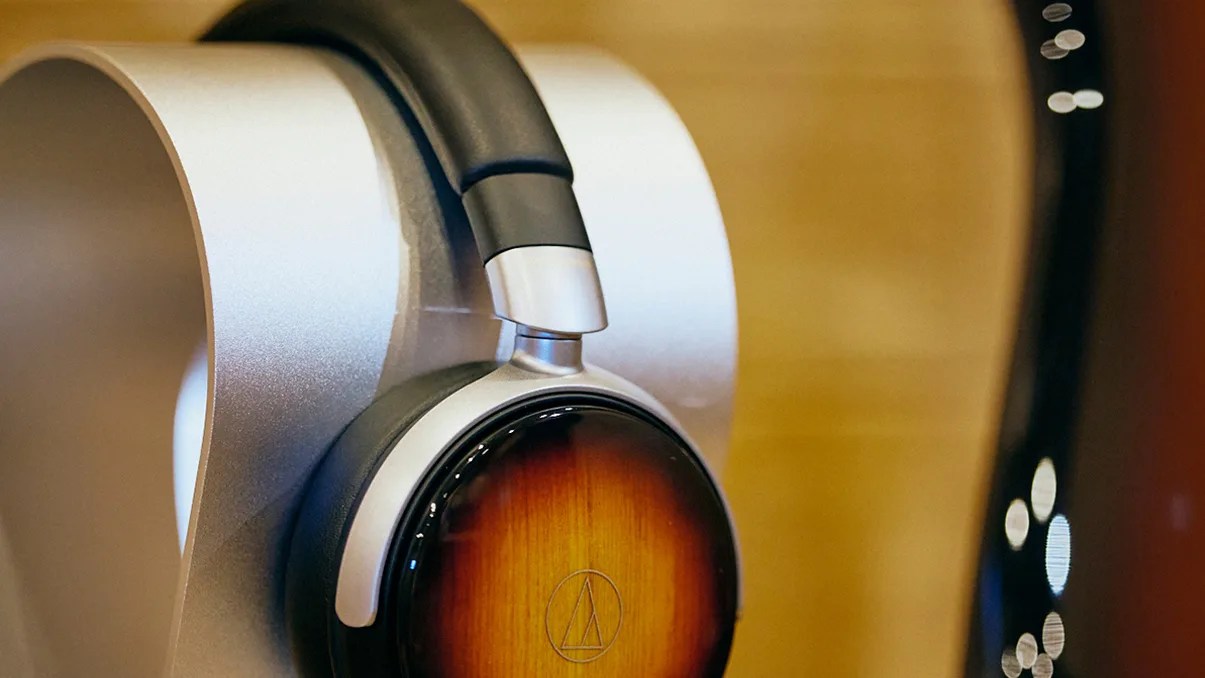 Over-ear headphones with wood-finish ear cups and black padded headband on a silver stand.