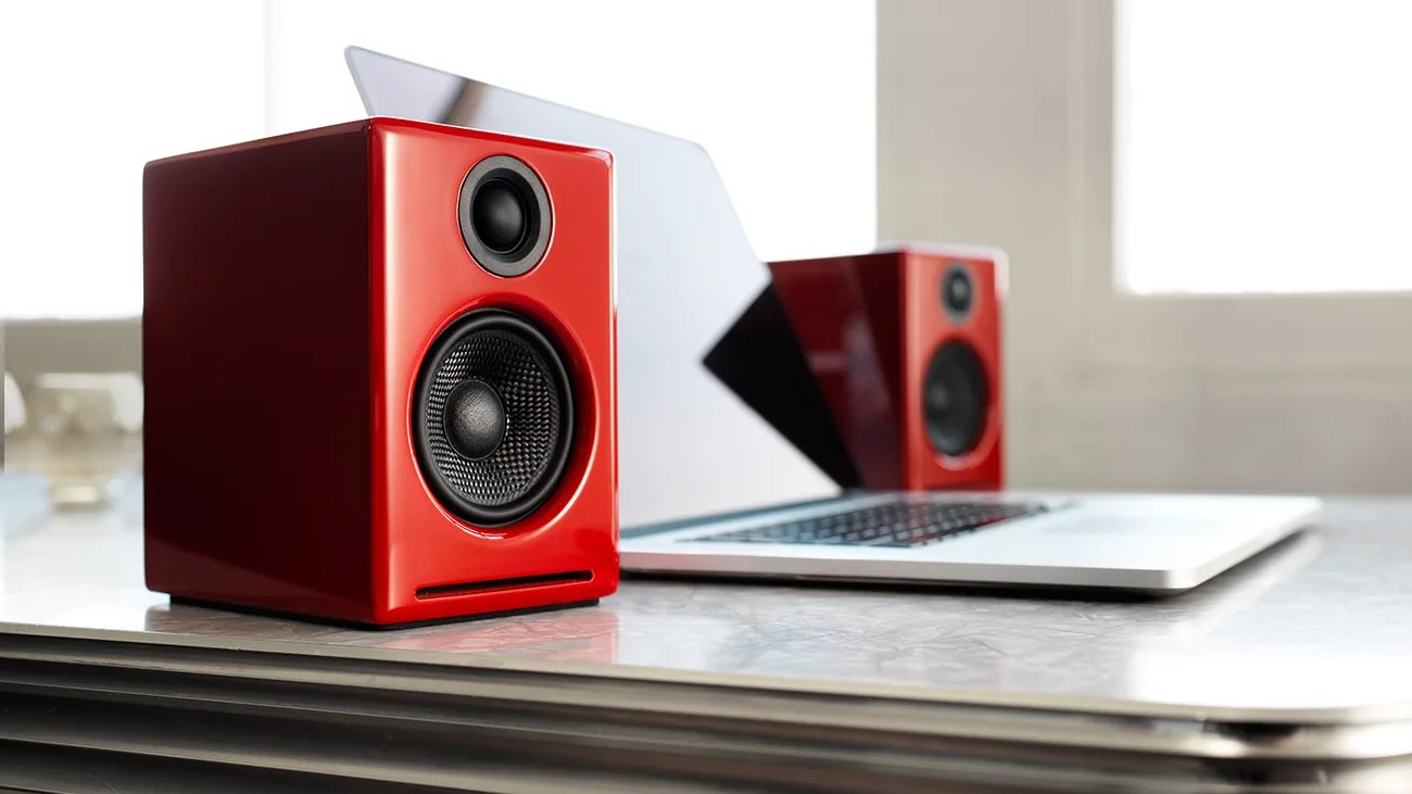 Pair of glossy red bookshelf speakers placed on either side of a silver laptop on a desk.