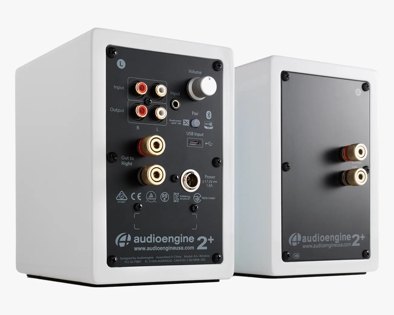 Pair of white Audioengine 2+ speakers showing rear panels with various input/output ports and volume knob.