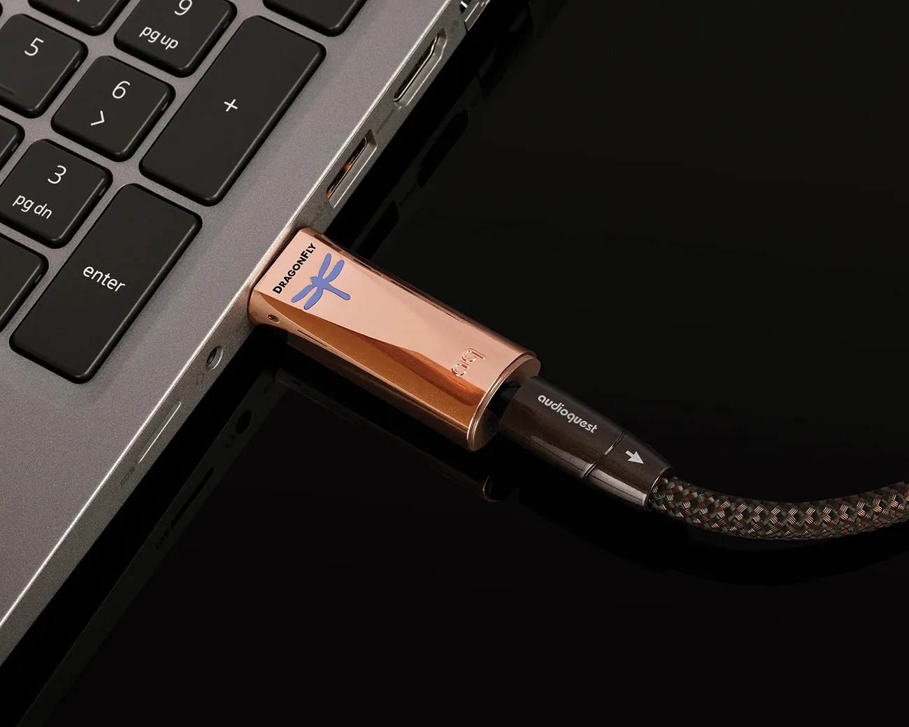Copper-colored DragonFly USB DAC connected to a laptop USB port with a braided AudioQuest cable.