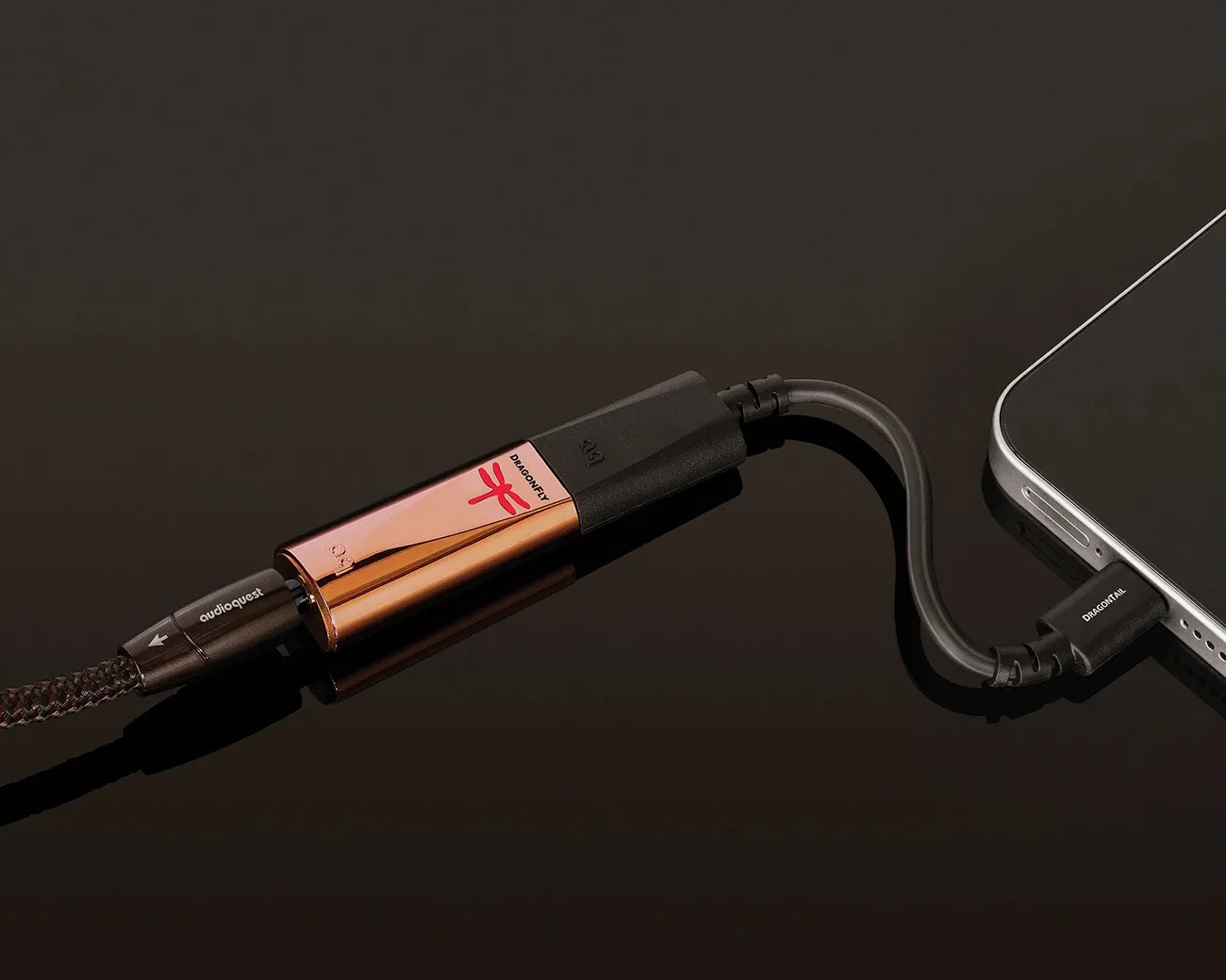 Copper-colored DragonFly USB digital-to-analog converter connected to a smartphone with black cables on a dark surface.