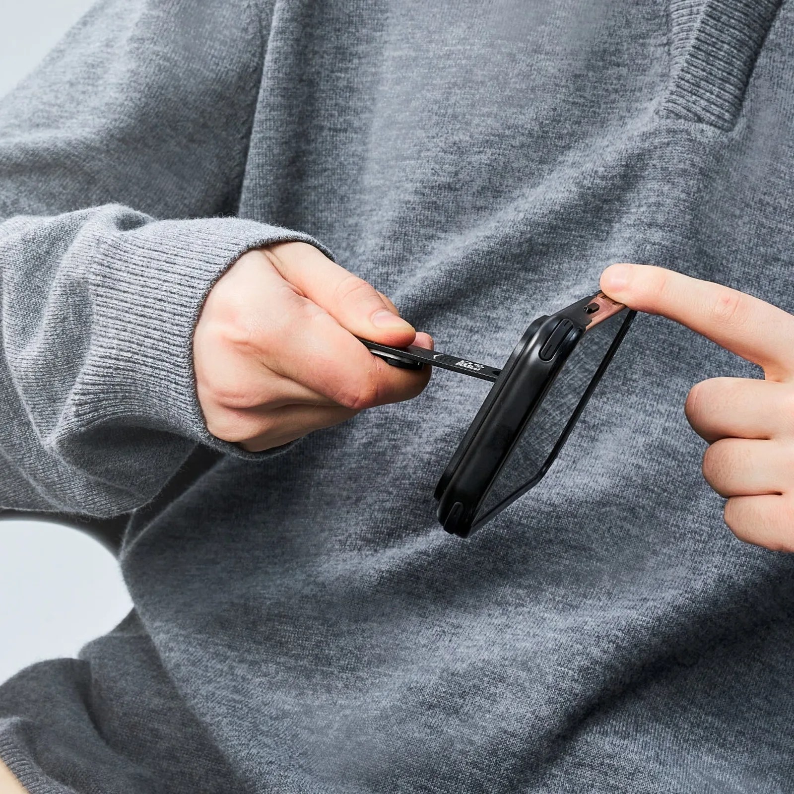 Person in a gray sweater inserting a SIM card into a black smartphone.