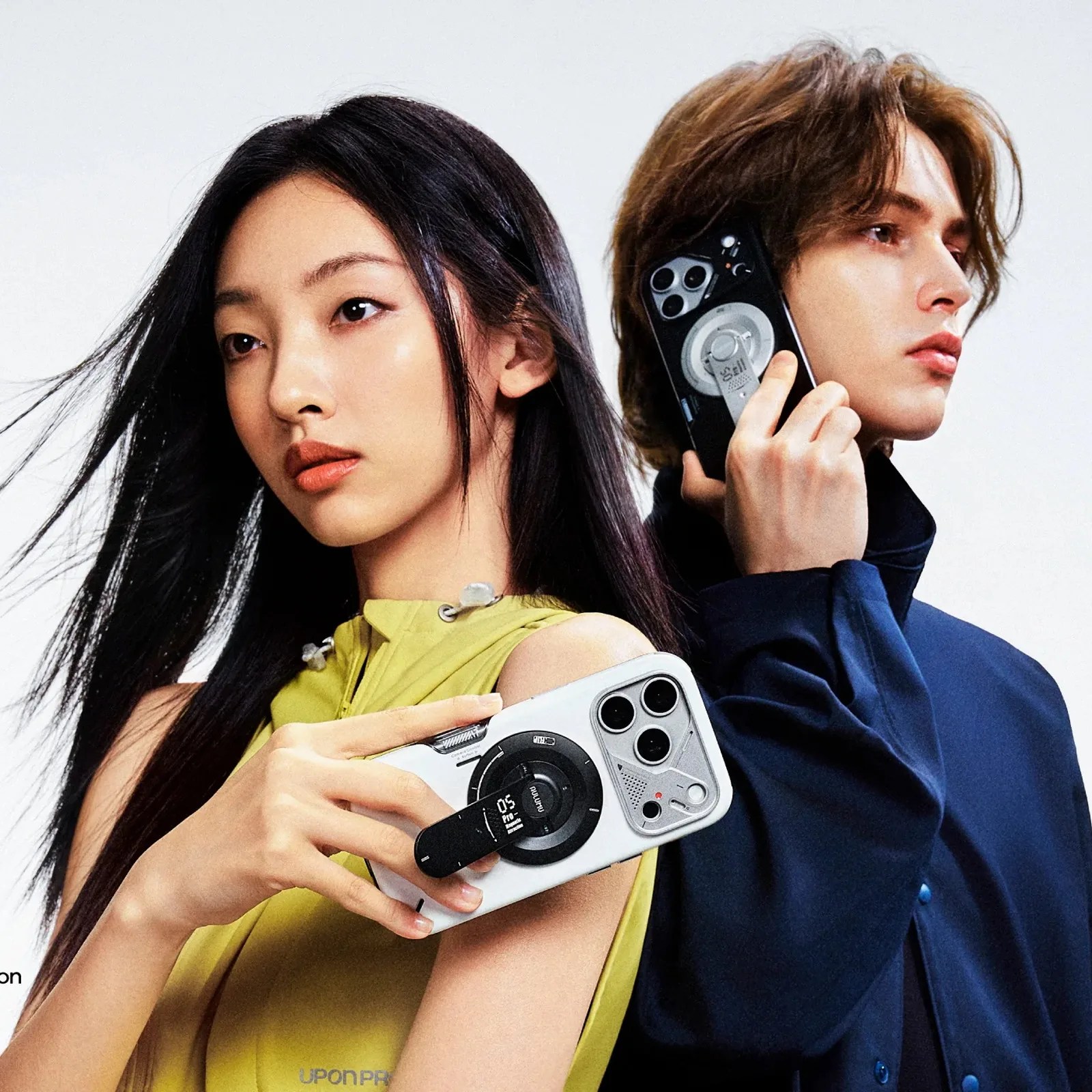 Two people holding smartphones with large circular camera modules and attached black accessories, one in a yellow sleeveless top and the other in a dark blue jacket.
