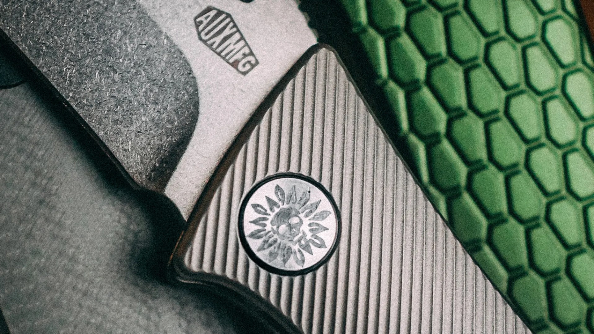 Close-up of a textured gray and green object with a circular emblem featuring a sun design and the text "AUXMFG.