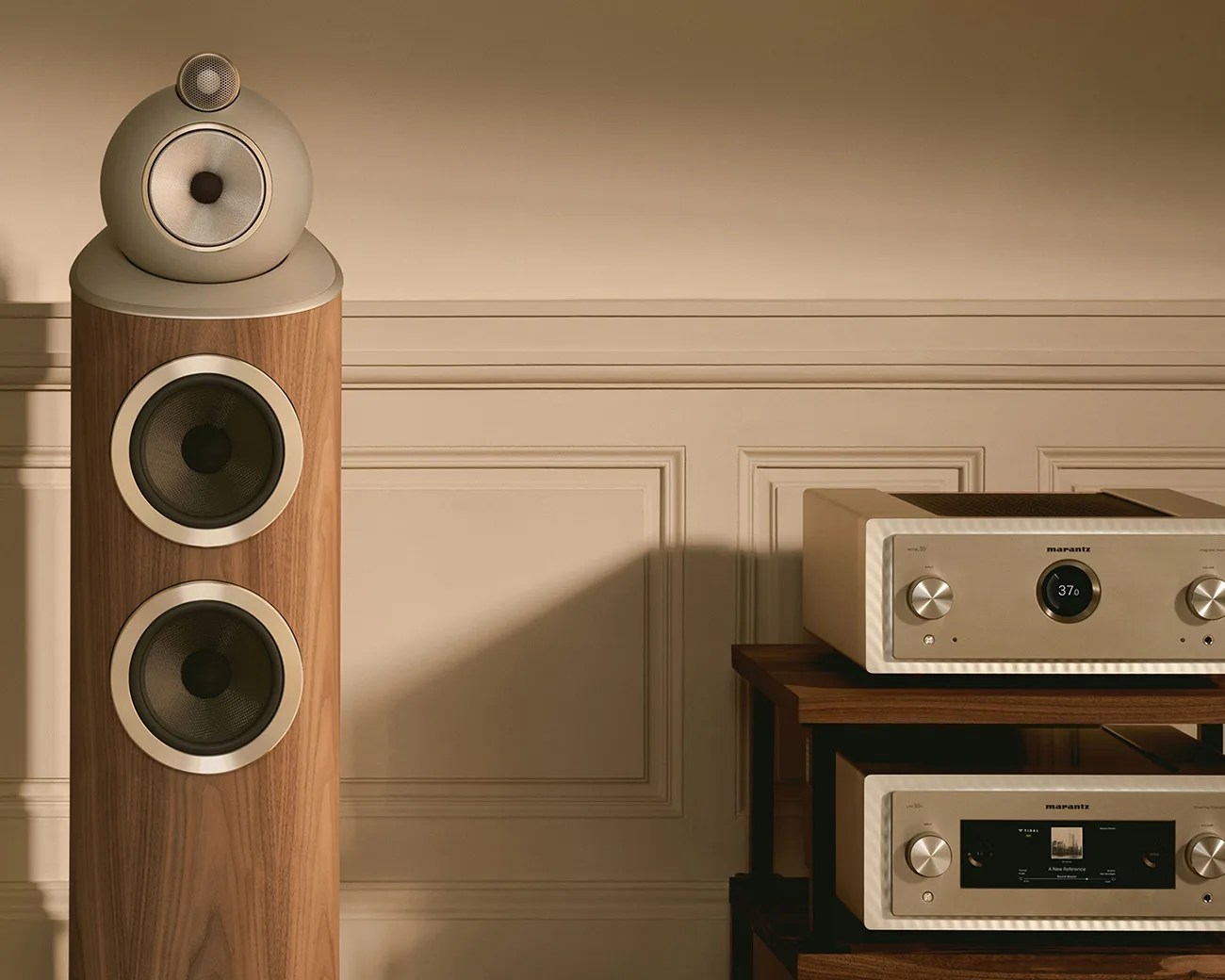 Tall wooden floor-standing speaker with beige drivers next to two beige Marantz audio components on a wooden shelf.